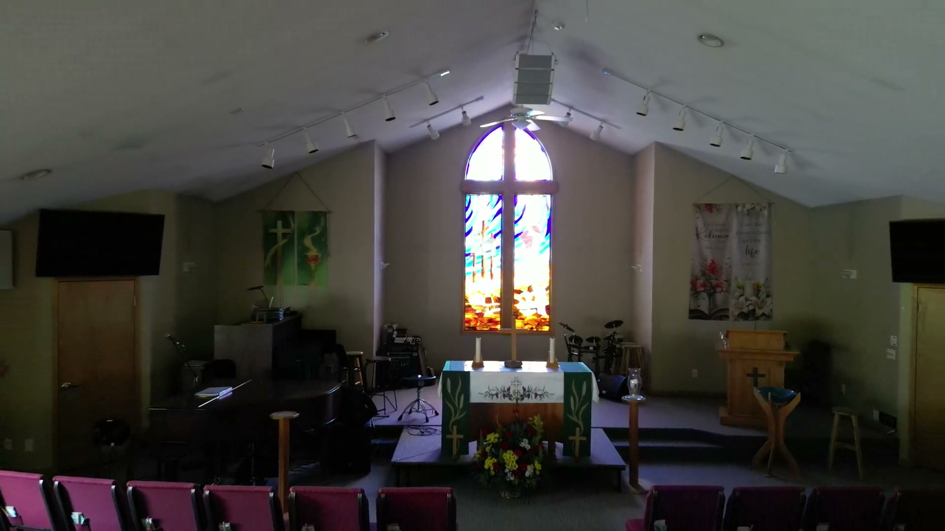 One take pulling back from the stained-glass window at St. Peter's until the whole sanctuary is in frame — the vaulted ceiling, both banners, the screens and every chair