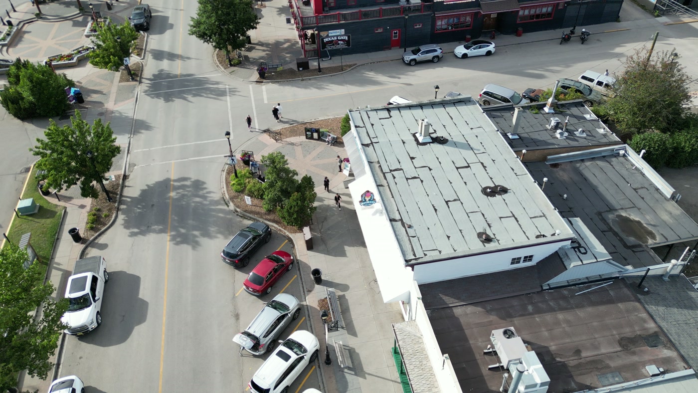 The shop's flat roof and white awning from above, cars angled along the street in front of it