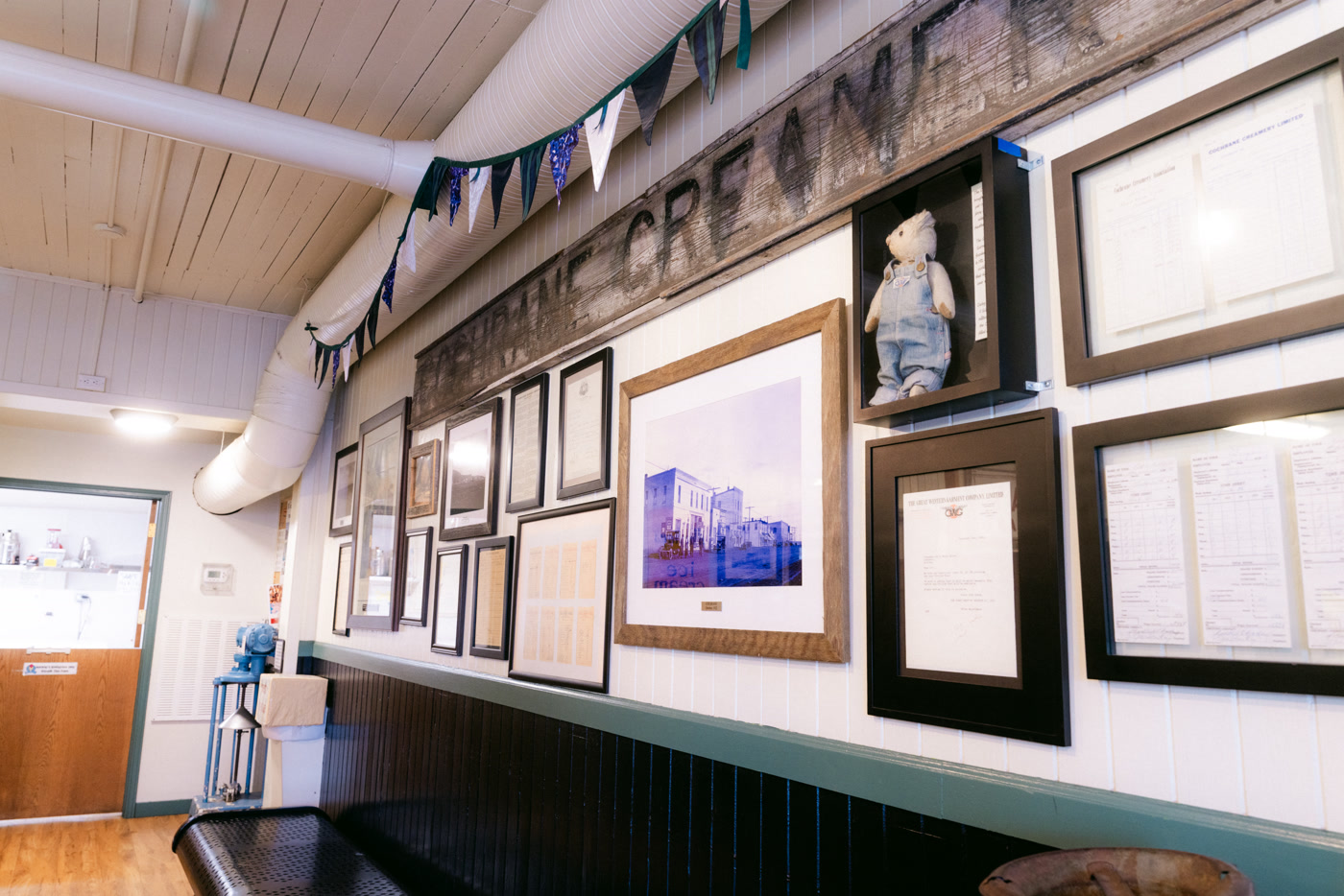 A long white-panelled wall of framed photographs and documents from the shop's past, bunting strung above it