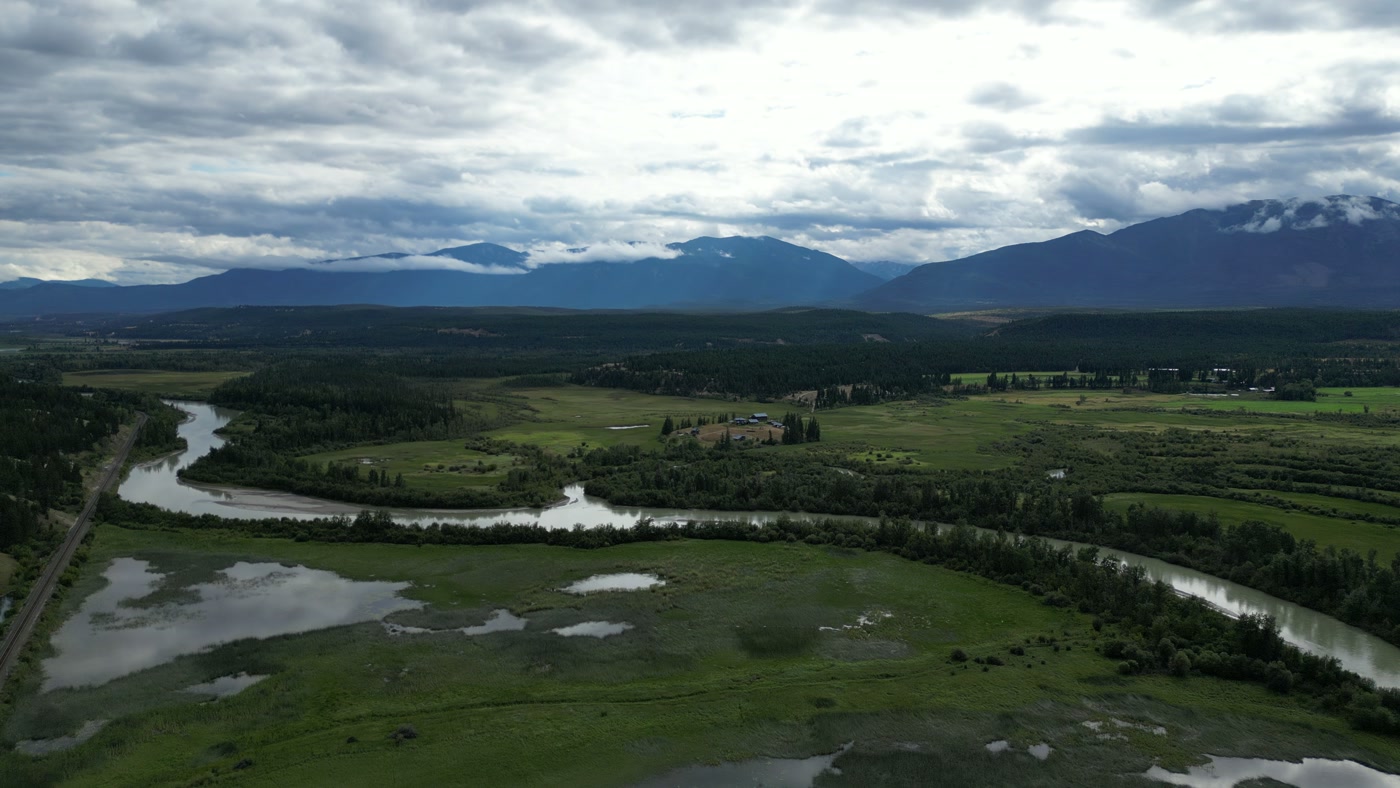 A single-track railway on a straight embankment along the edge of the Columbia wetland at Radium Hot Springs, the river and its oxbows on the far side