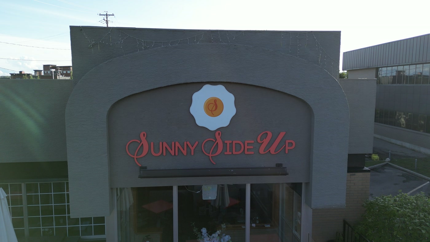 The Sunny Side Up sign in Cochrane close up: a scalloped white egg with a script S in its orange yolk, red letters with script capitals beneath, small bulbs along the grey parapet