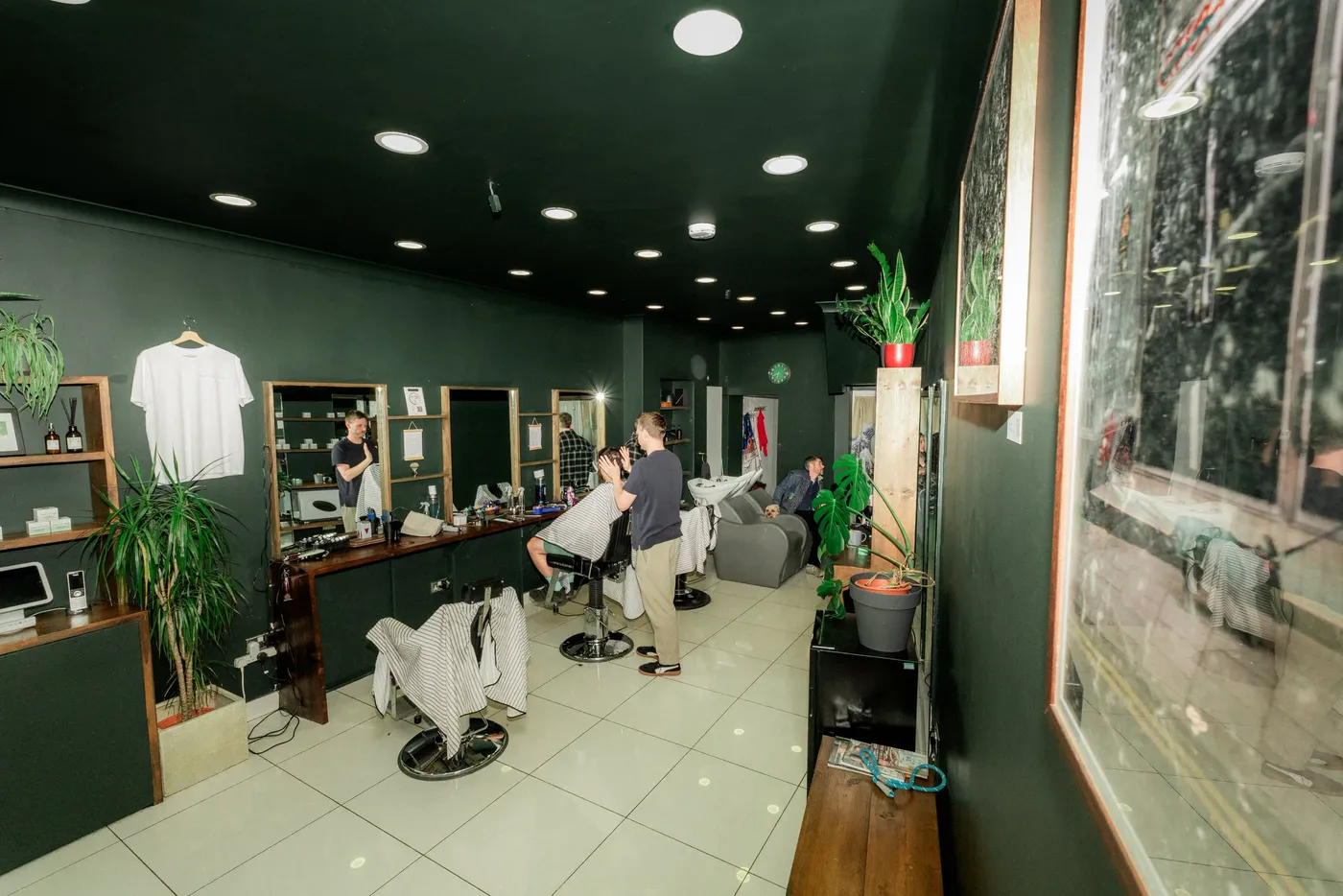 A dark green barbershop interior with a client in the chair and mirrors along the wall