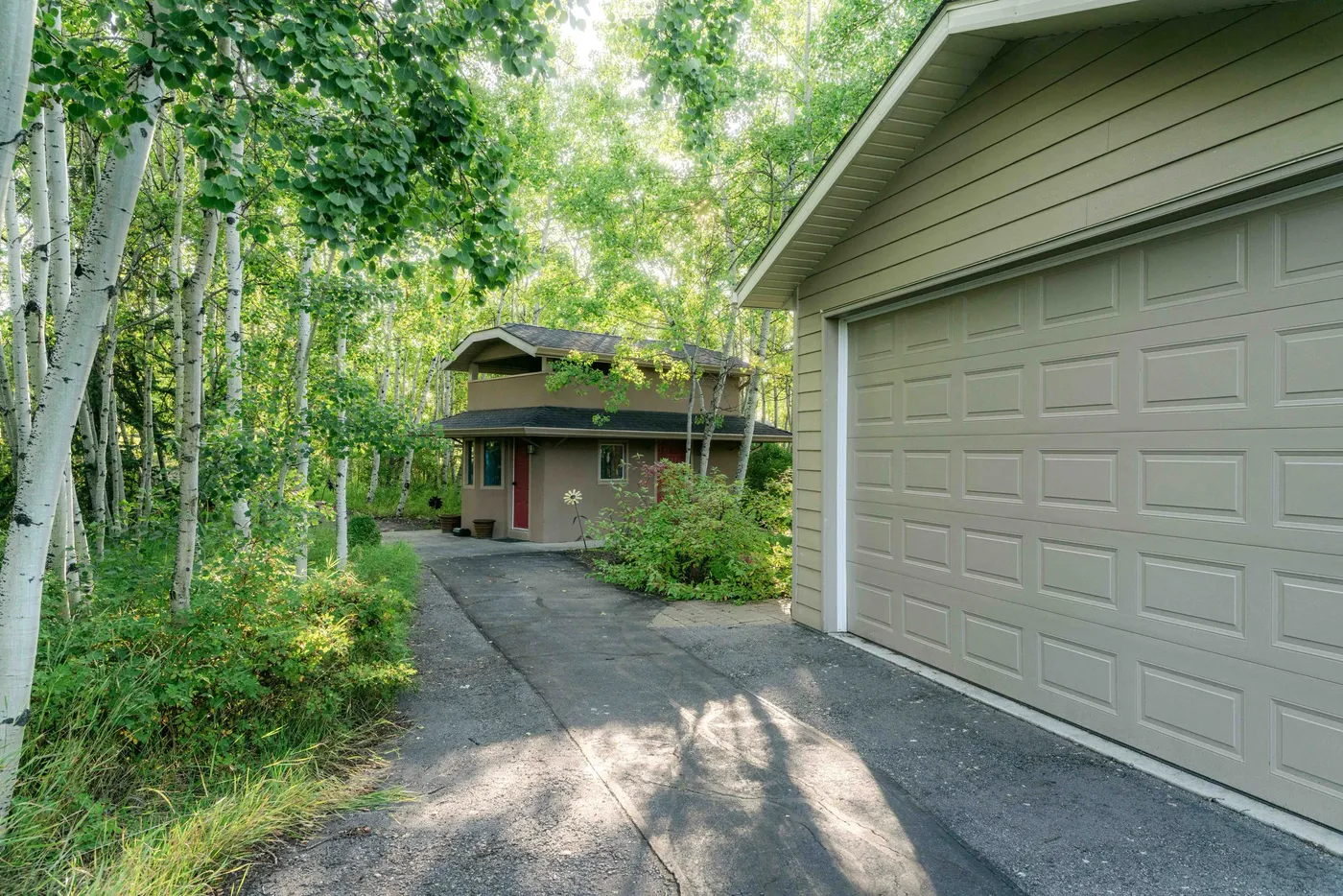 A house at the end of a curving driveway framed by aspens, garage door closed