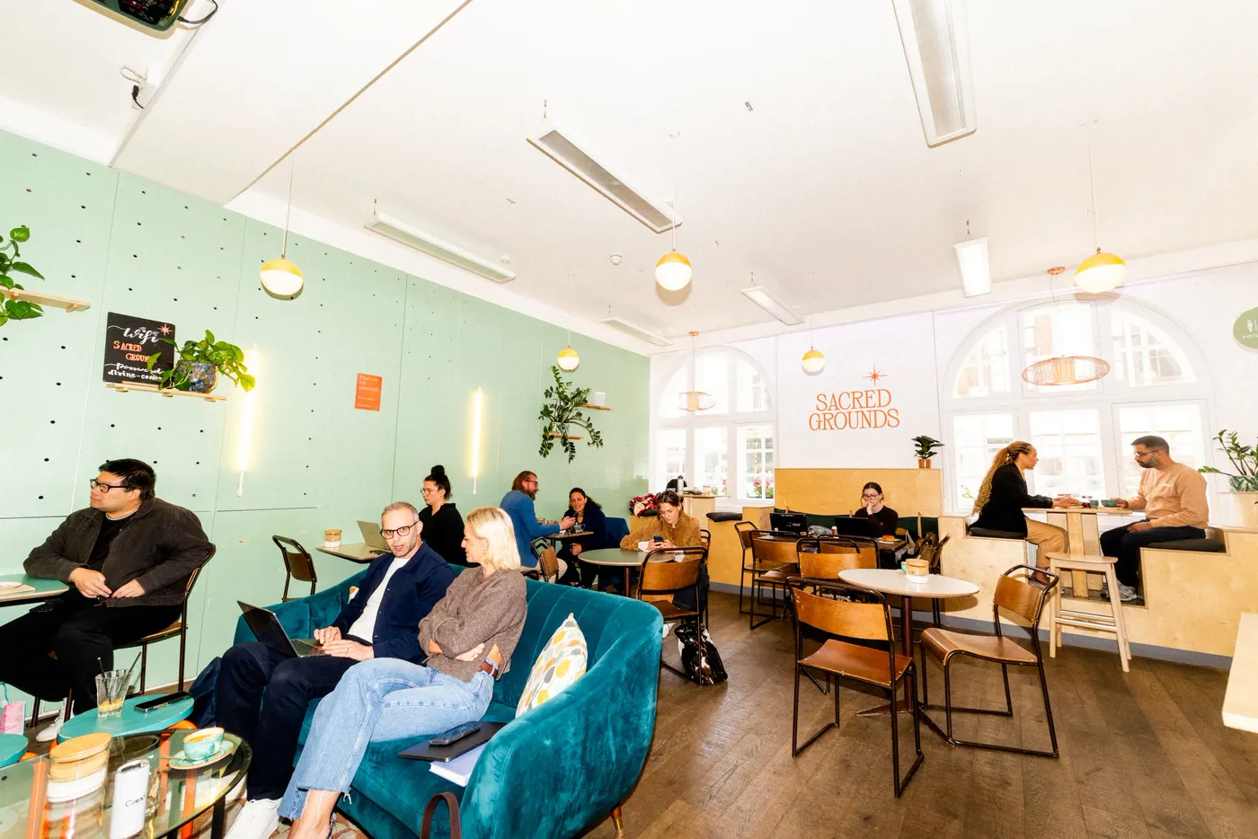 A green-walled cafe with guests working across sofas, stools and small tables