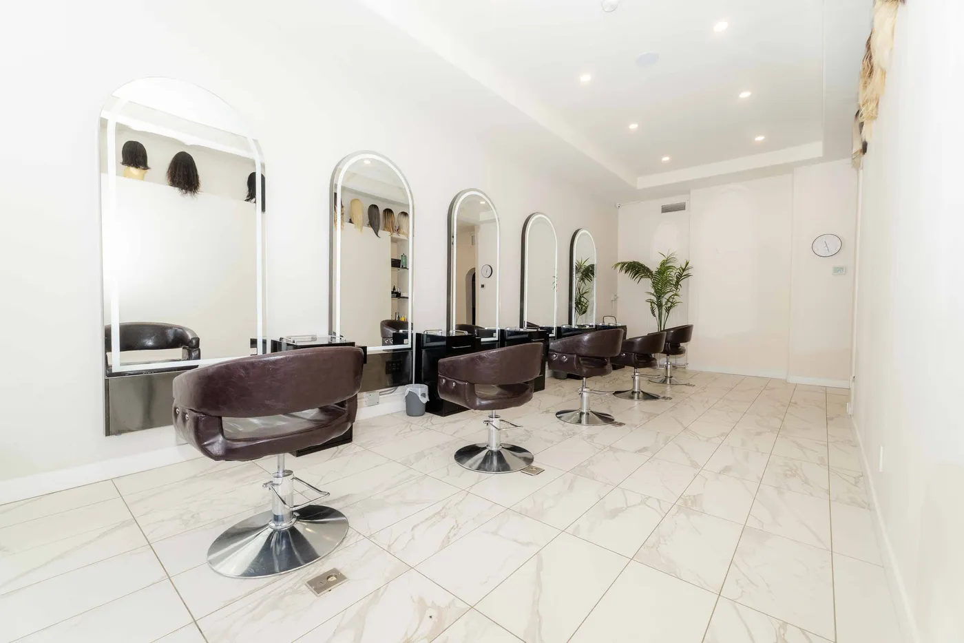 A row of arched mirrors and styling chairs in a white marble salon