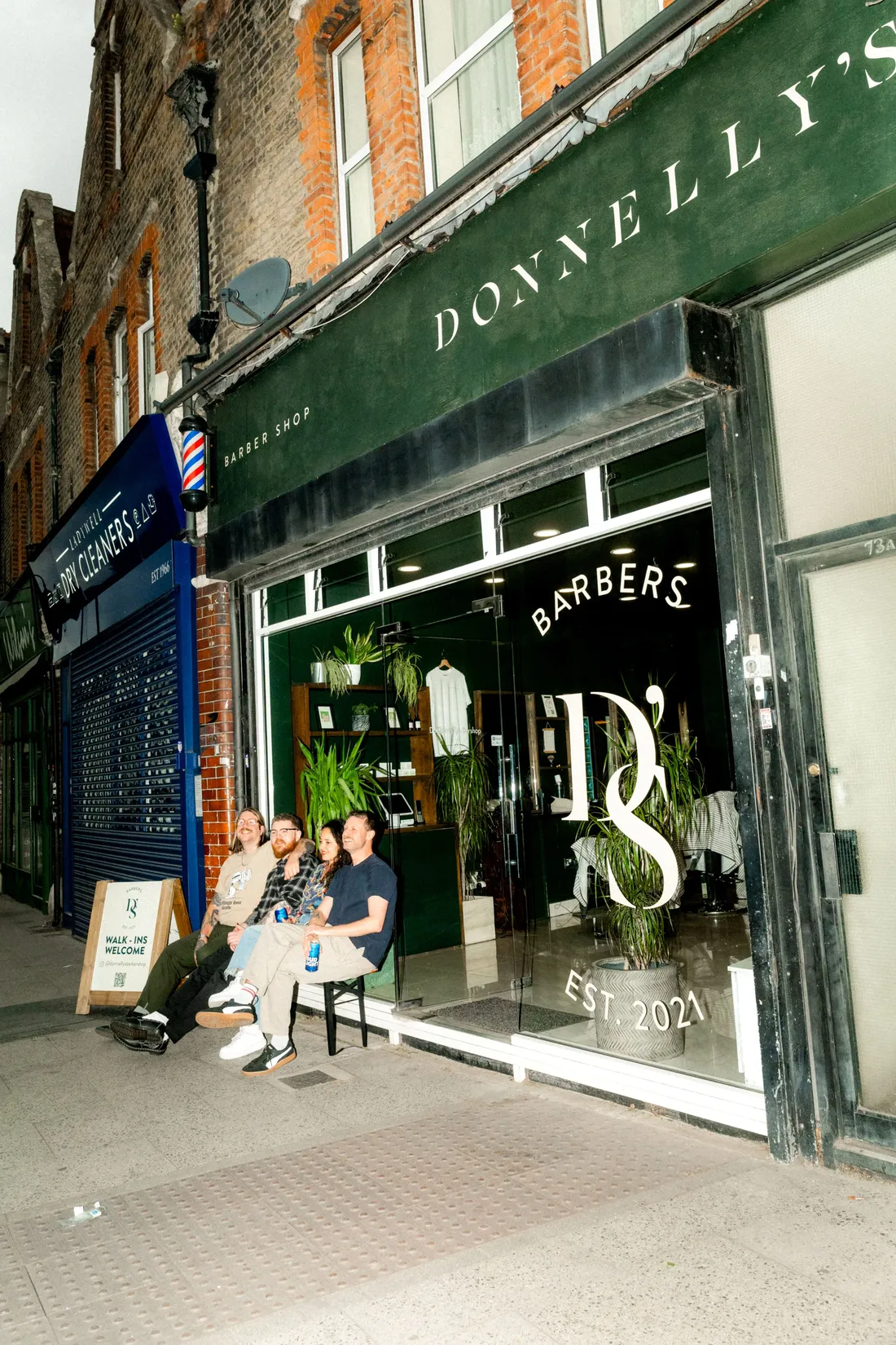 A barbershop storefront in a brick heritage building, three people sitting outside