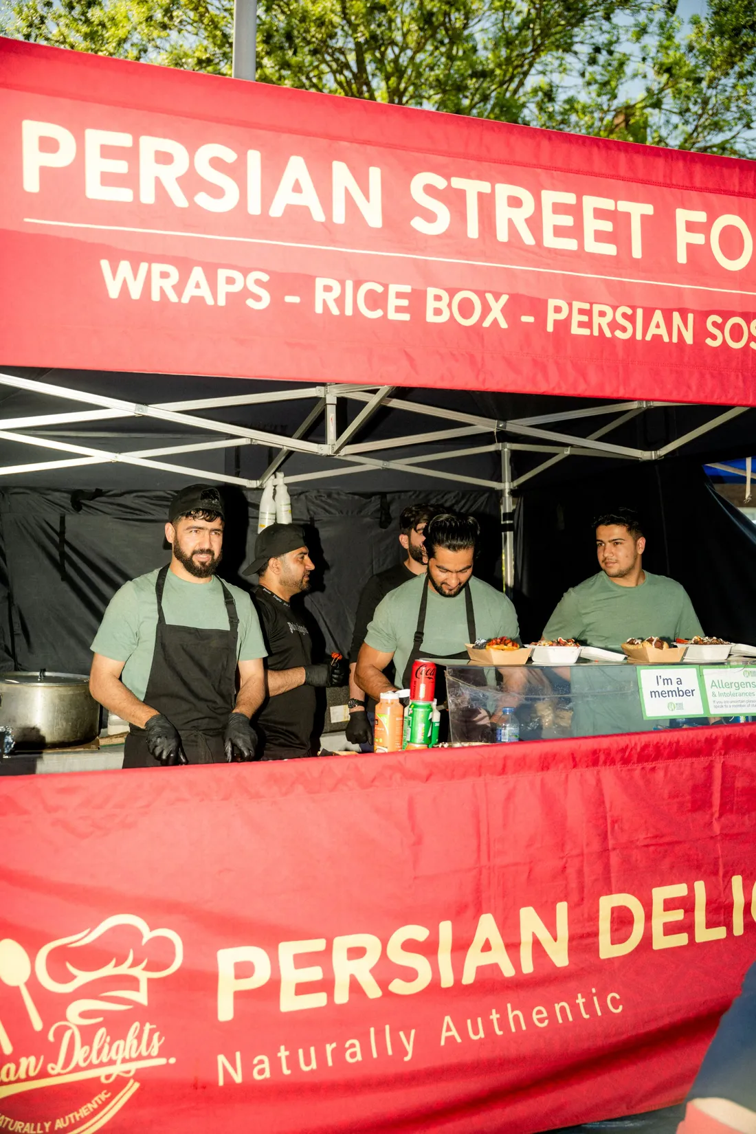 Cooks working behind a red-canopied Persian street food stall