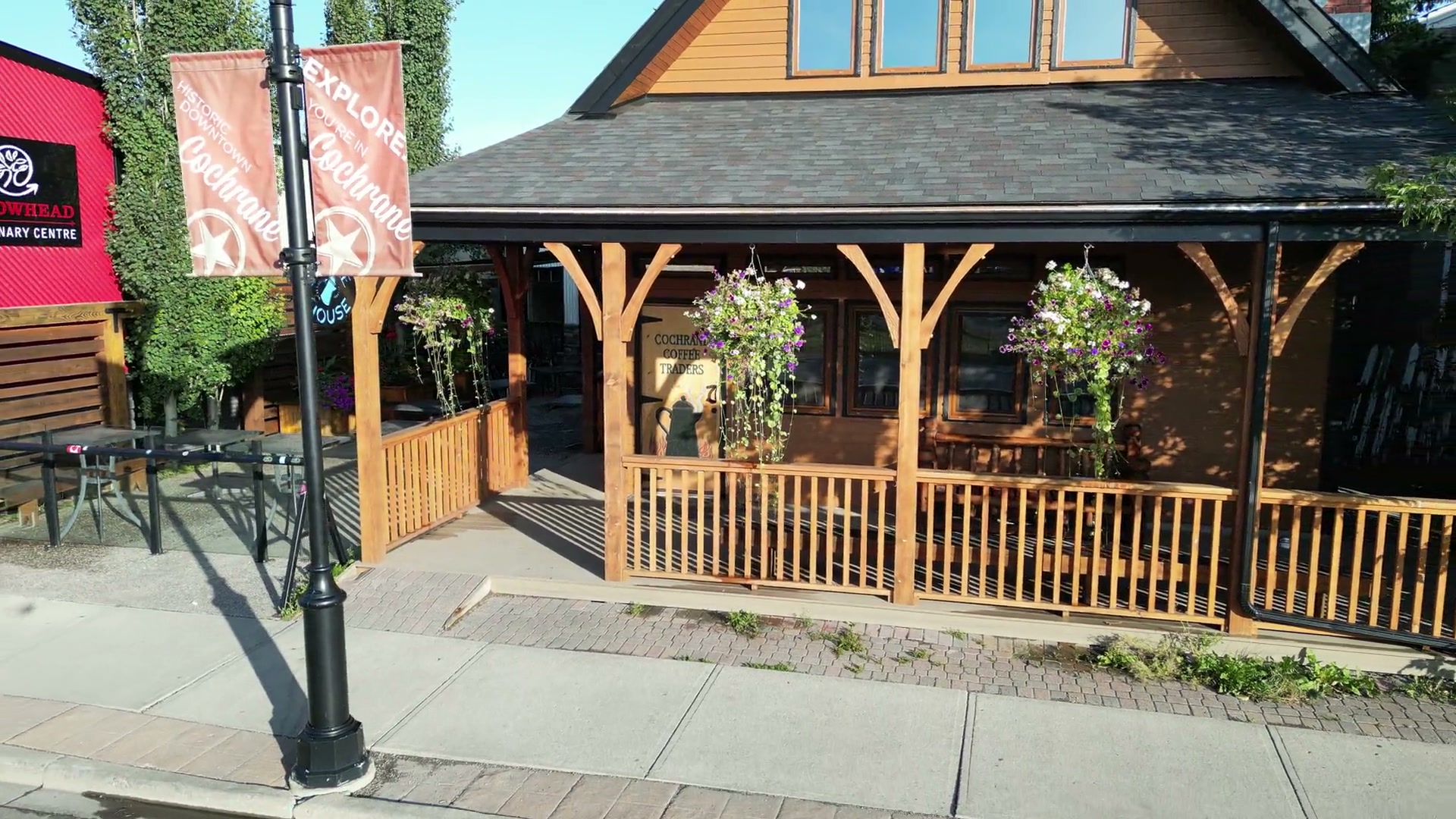 Drifting back from the porch of Cochrane Coffee Traders past its round Coffee House sign to a black lamp post on 2nd Avenue West, its two salmon Cochrane banners, and the red clinic next door