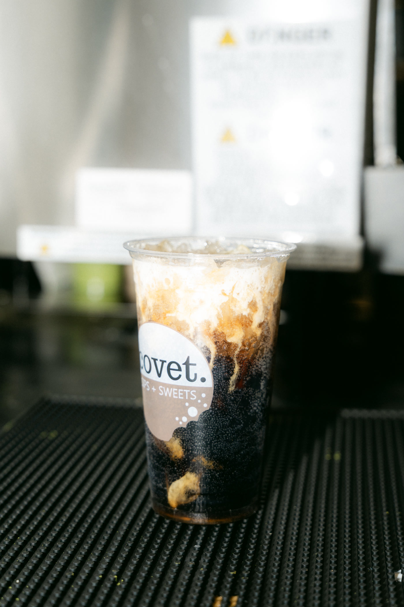 An iced drink with dark swirls through the cream, set down on a black bar mat inside Covet Sips + Sweets in Cochrane