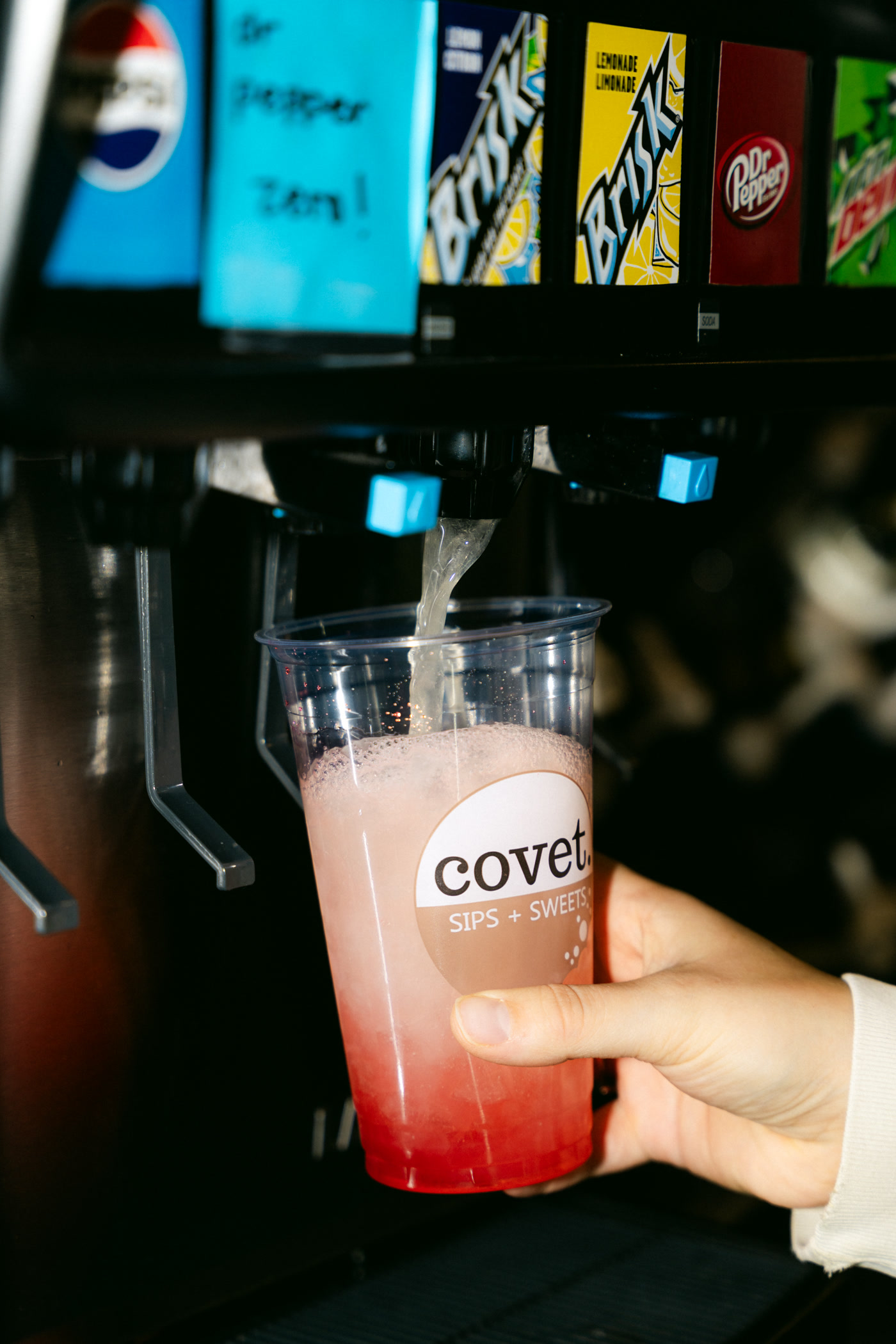 The pop fountain inside Covet Sips + Sweets in Cochrane pouring into a clear covet cup already layered pink and red