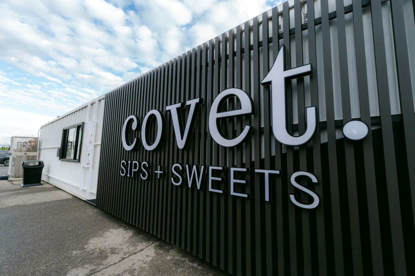 The name on the Covet Sips + Sweets container in Cochrane: covet. in white on black vertical slats, SIPS + SWEETS beneath it