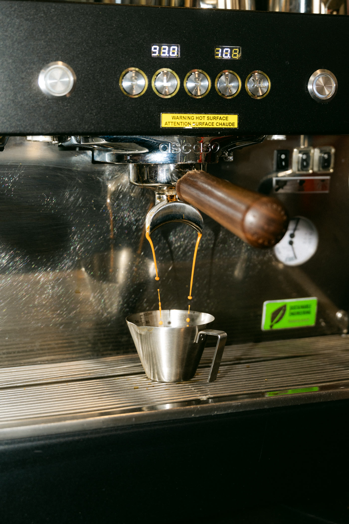 Espresso running from a wooden-handled portafilter into a steel jug on the machine at Covet Sips + Sweets in Cochrane
