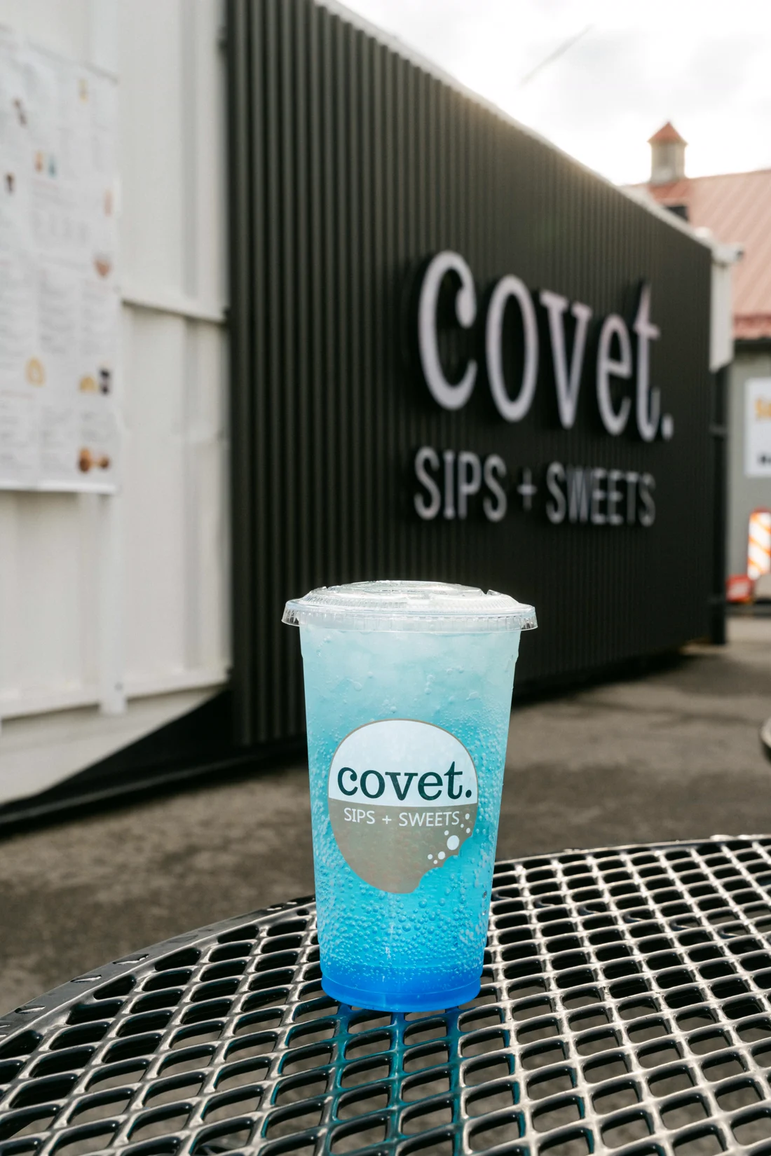 A bright blue slush drink on a mesh table outside a black kiosk