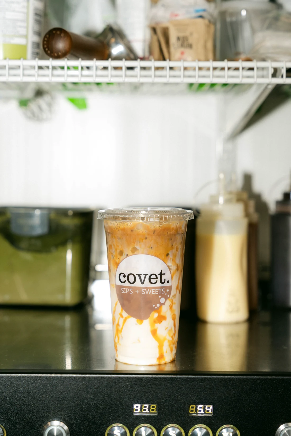 An iced latte swirled with caramel on a counter beside syrup bottles