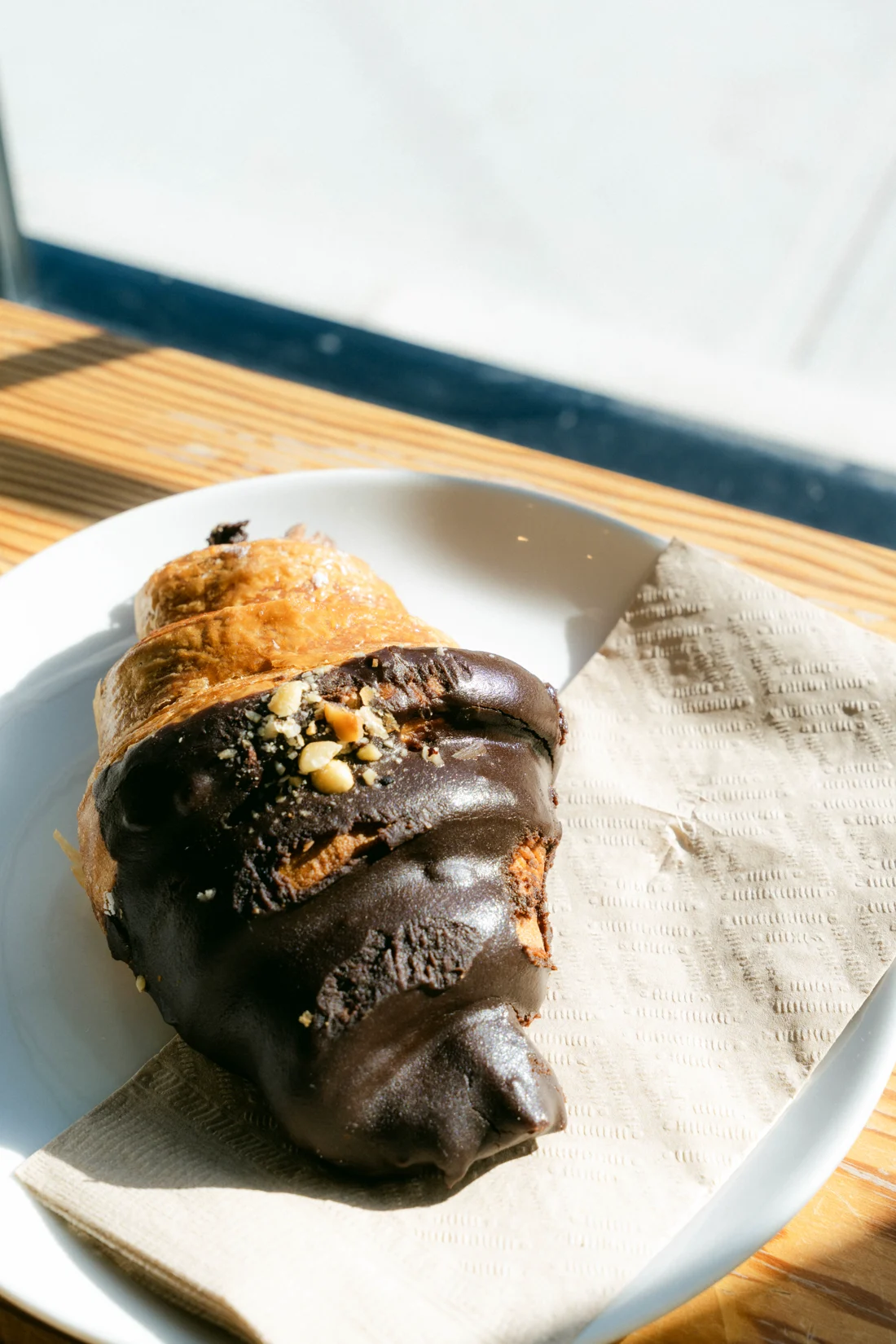 A chocolate-dipped croissant on a napkin and white plate on a wooden table