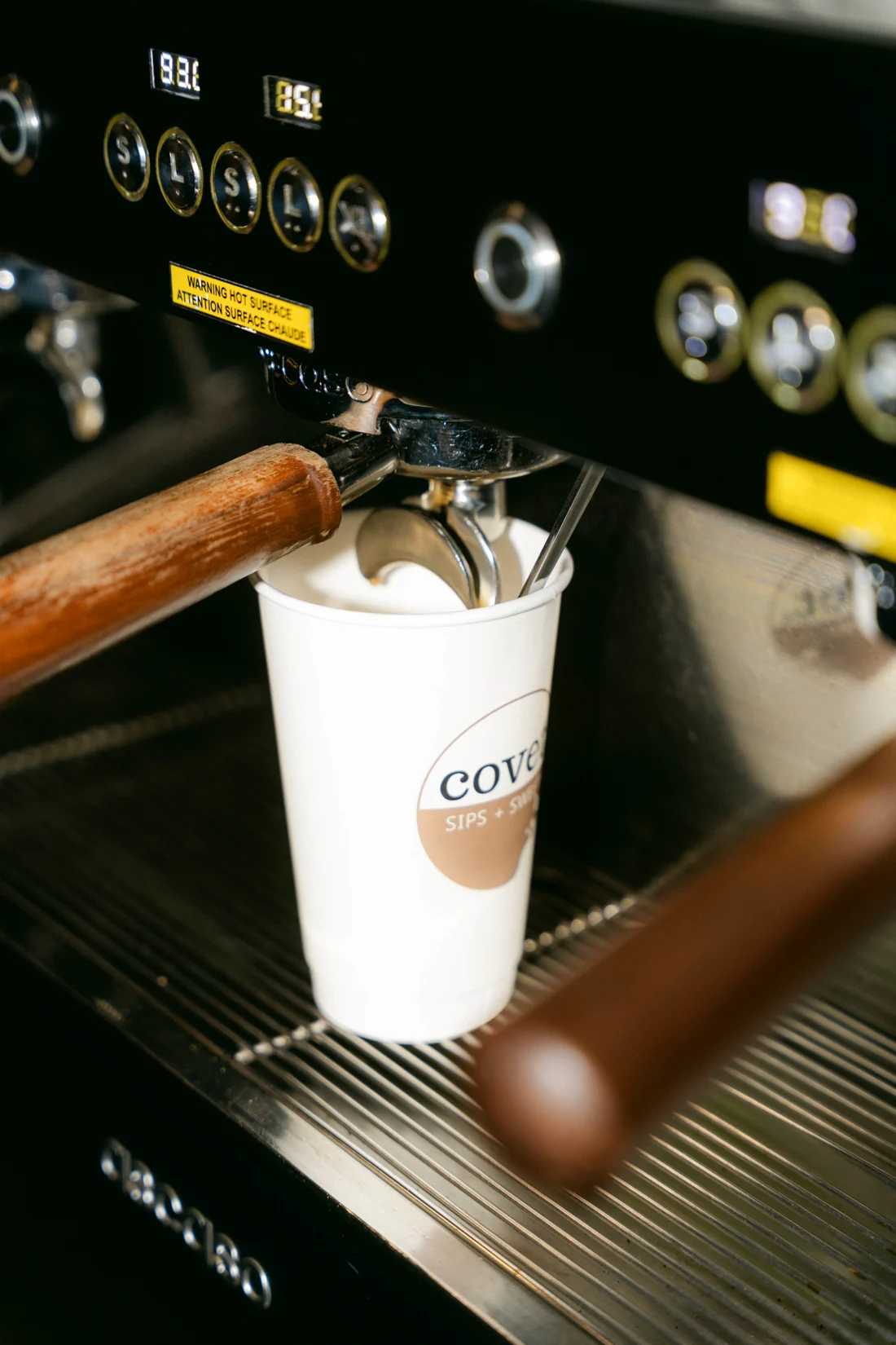 A portafilter drips espresso into a paper cup on a black machine