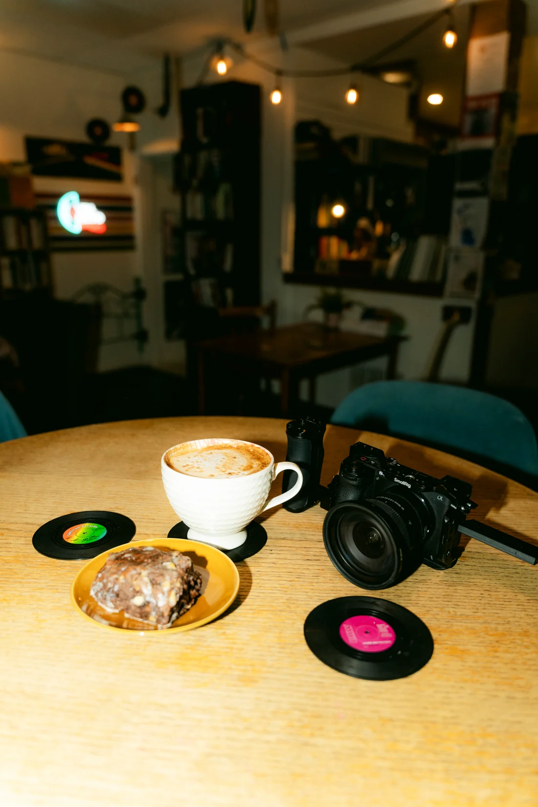 A latte, a cookie and a camera on a wooden table with vinyl records in a bookshop café