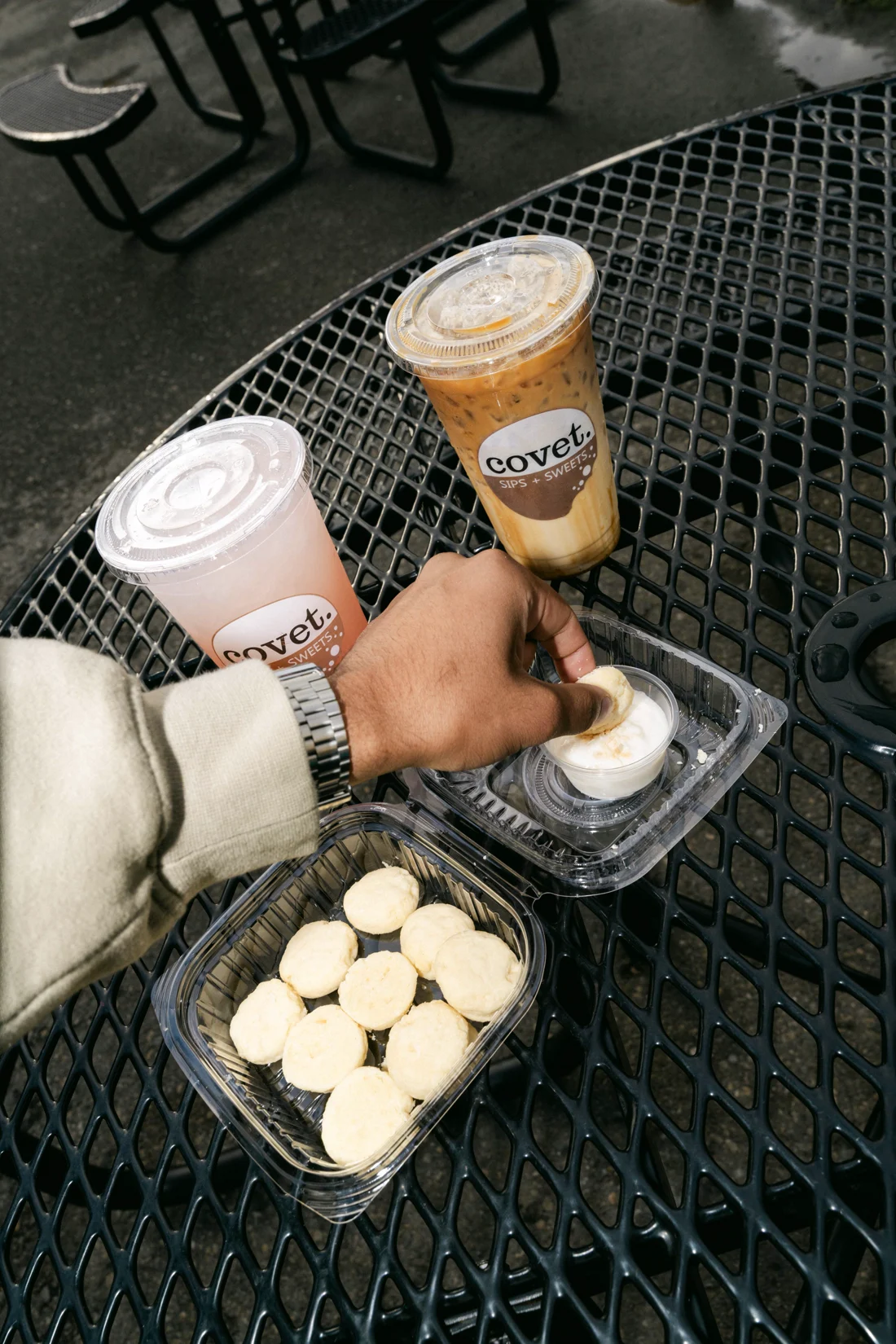 A hand reaches for mini cheesecakes beside two iced drinks on a tray