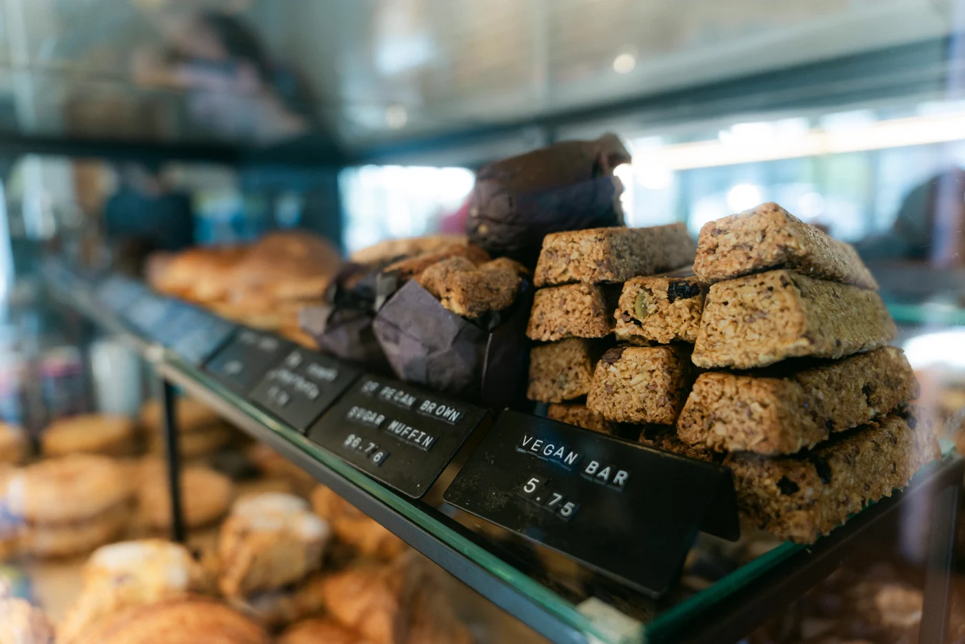 Date squares, brownies and pastries with chalkboard price tags behind the glass of a café case