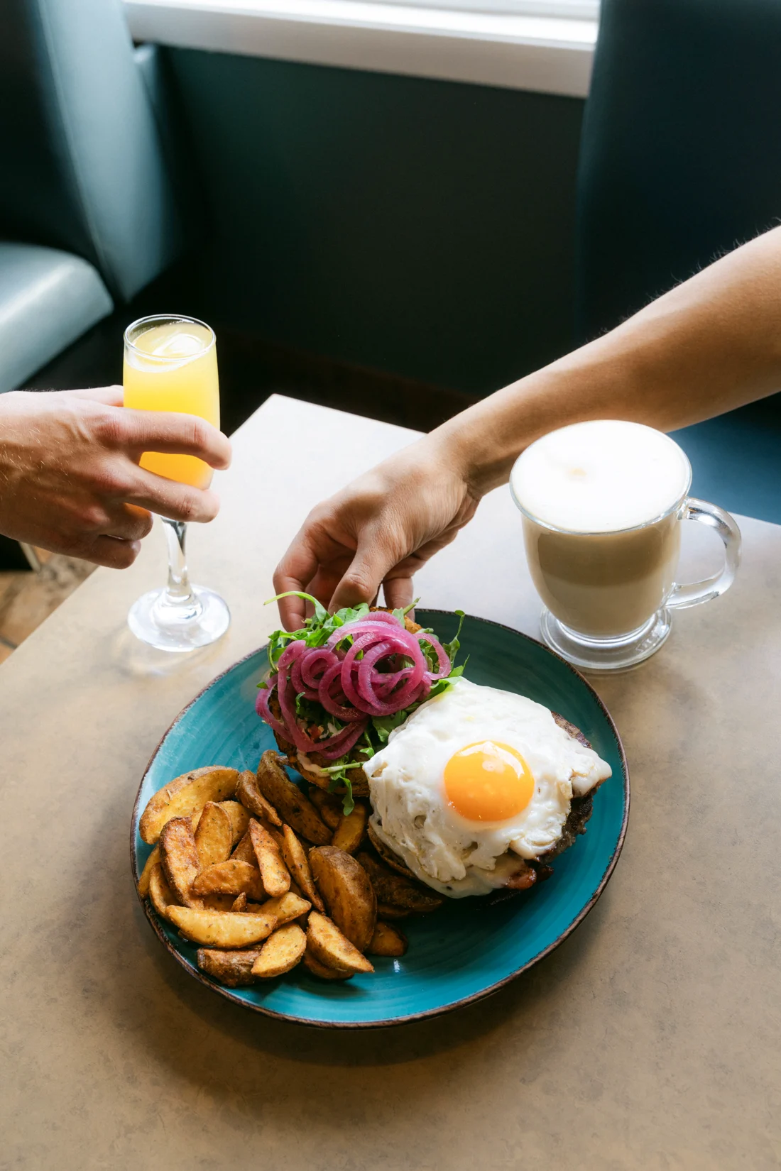A hand reaches for a plate of burger and wedges beside a mimosa