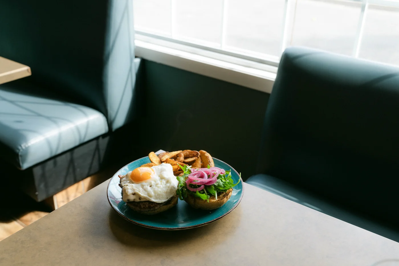 A teal plate of burger and wedges on a diner table between green booths