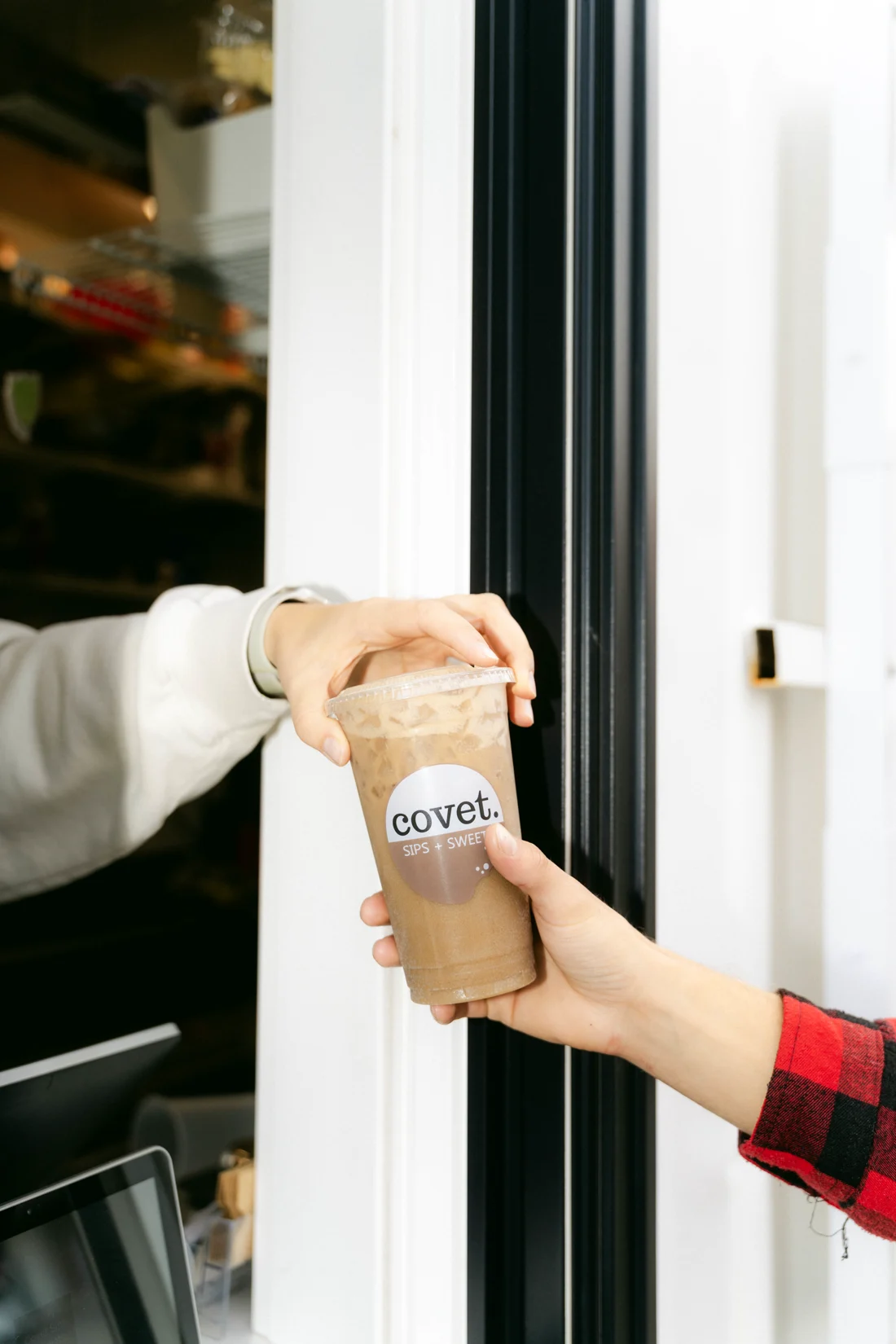An iced coffee handed through a takeout window to a customer in flannel