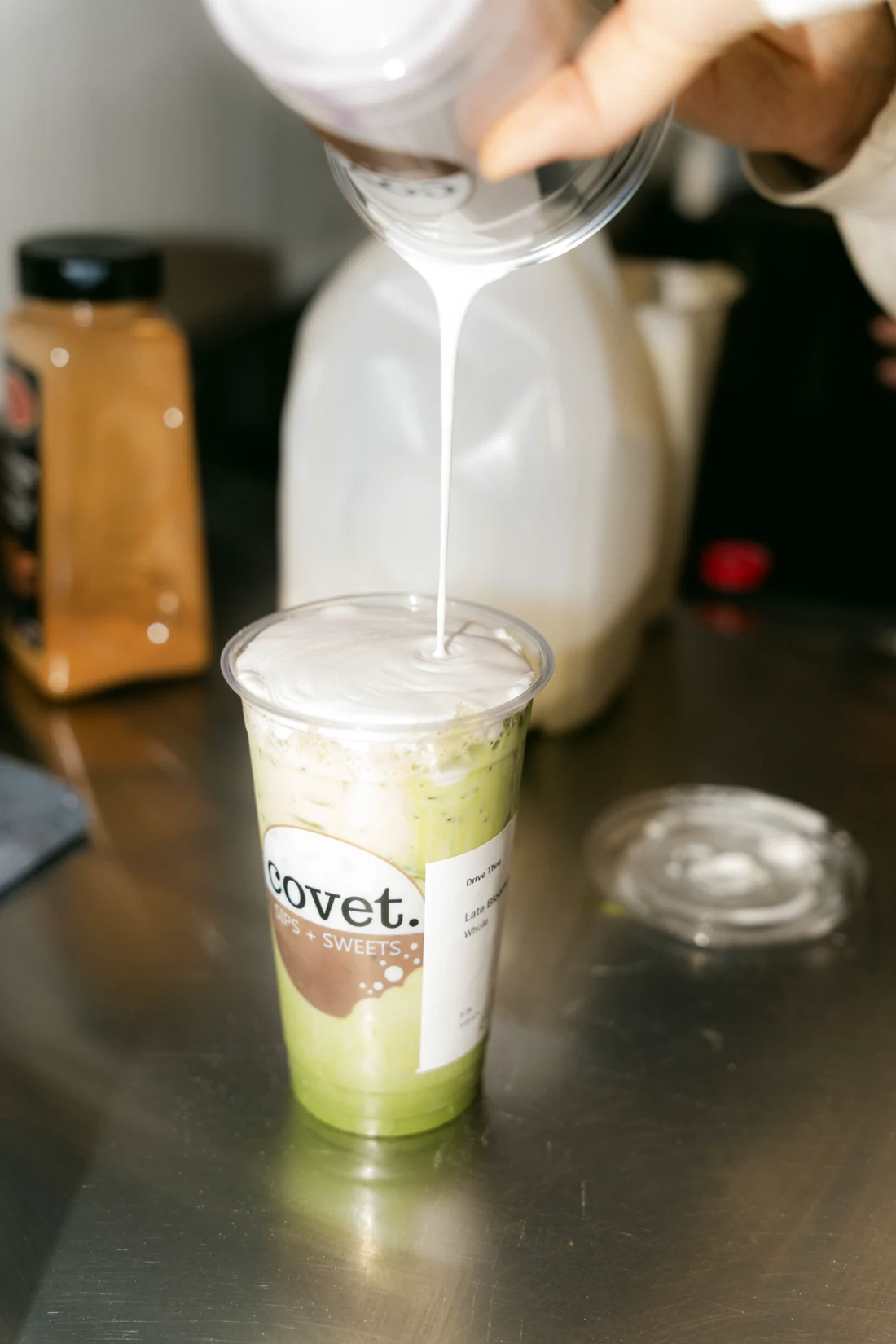 Milk pours from a jug into an iced matcha in a branded cup