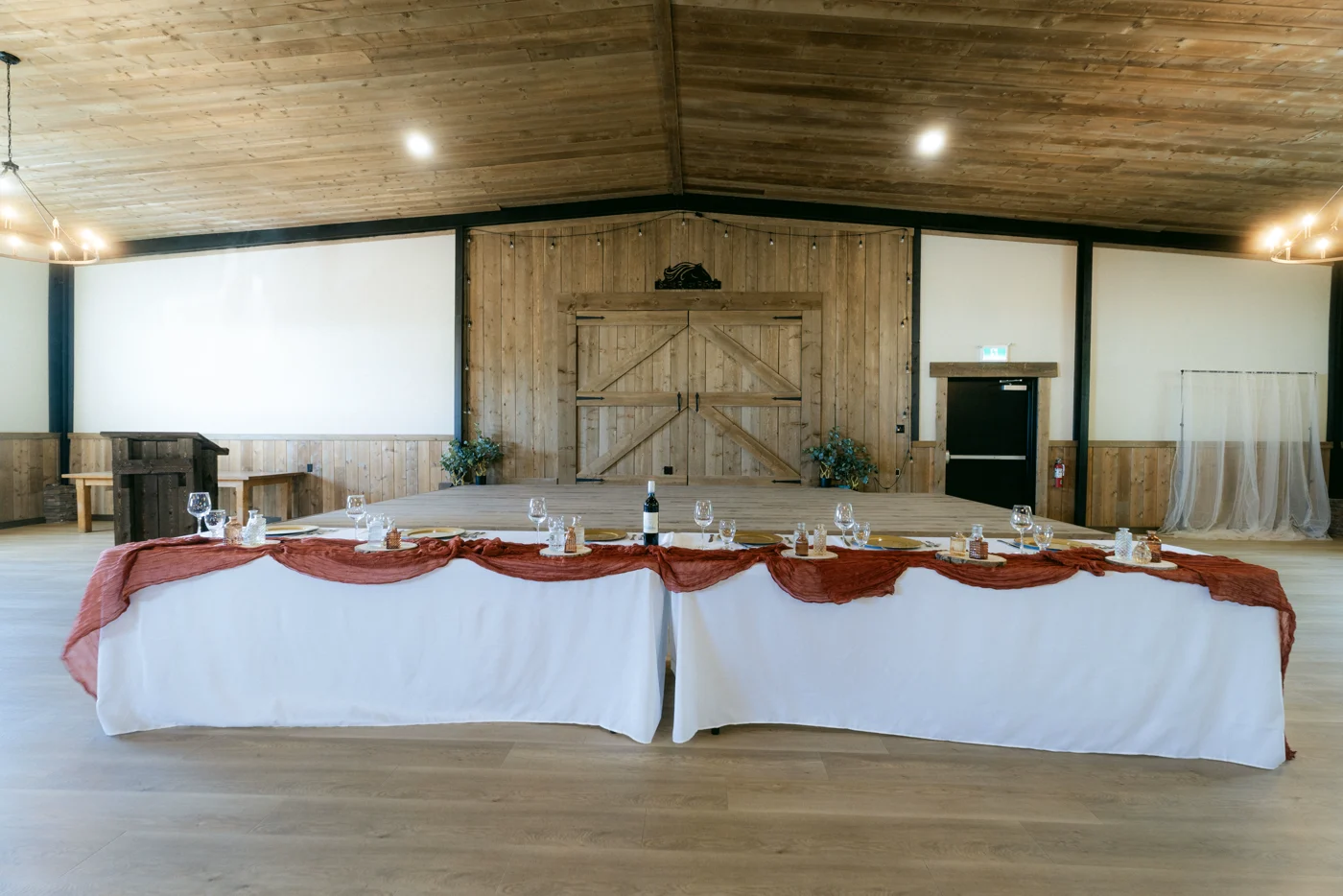 A head table in white linen before the closed barn doors of an event hall