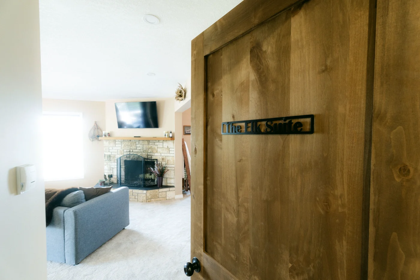 A wooden door with a plaque opens onto a suite with a stone fireplace