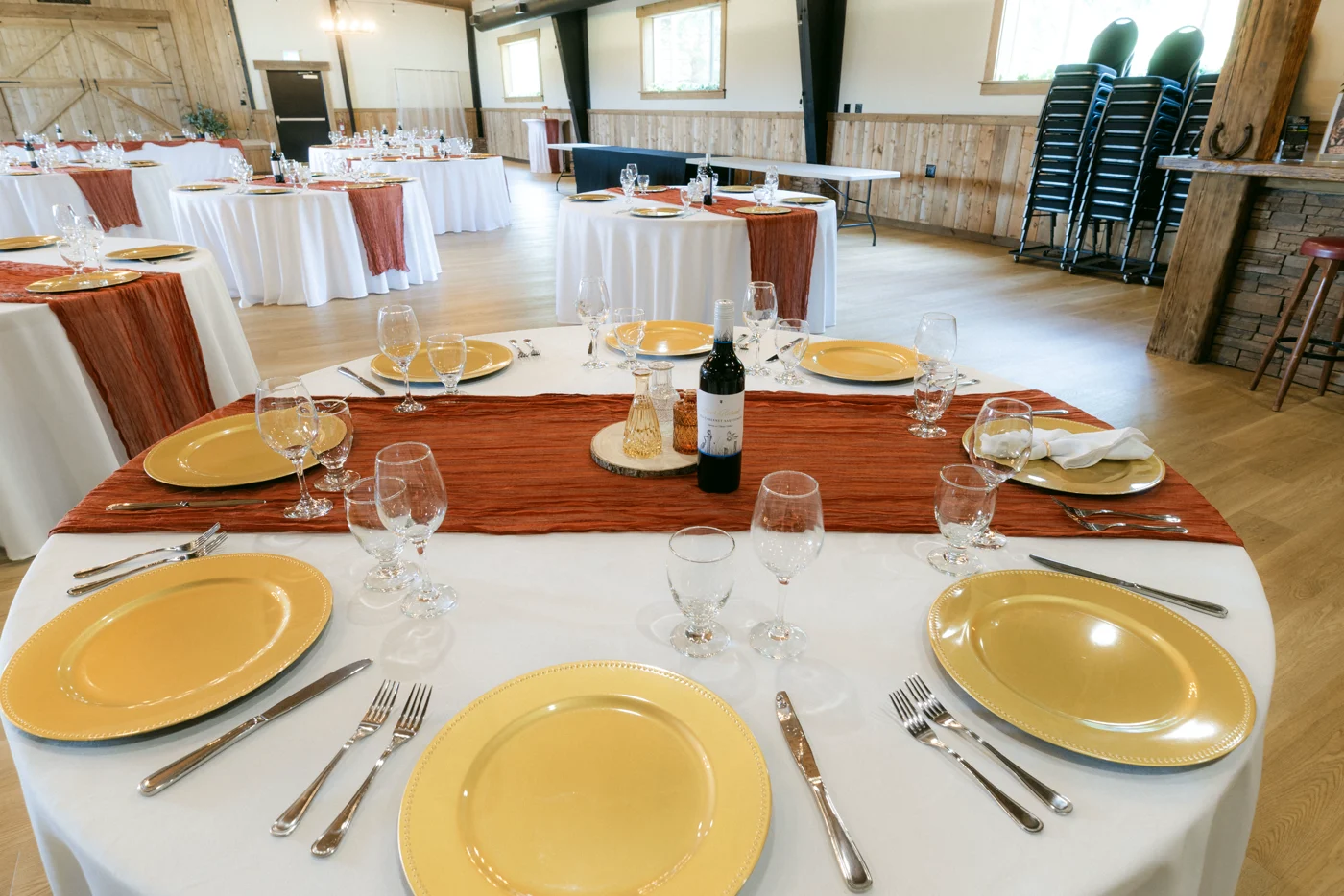 A round table set with gold chargers, glassware and a rust runner