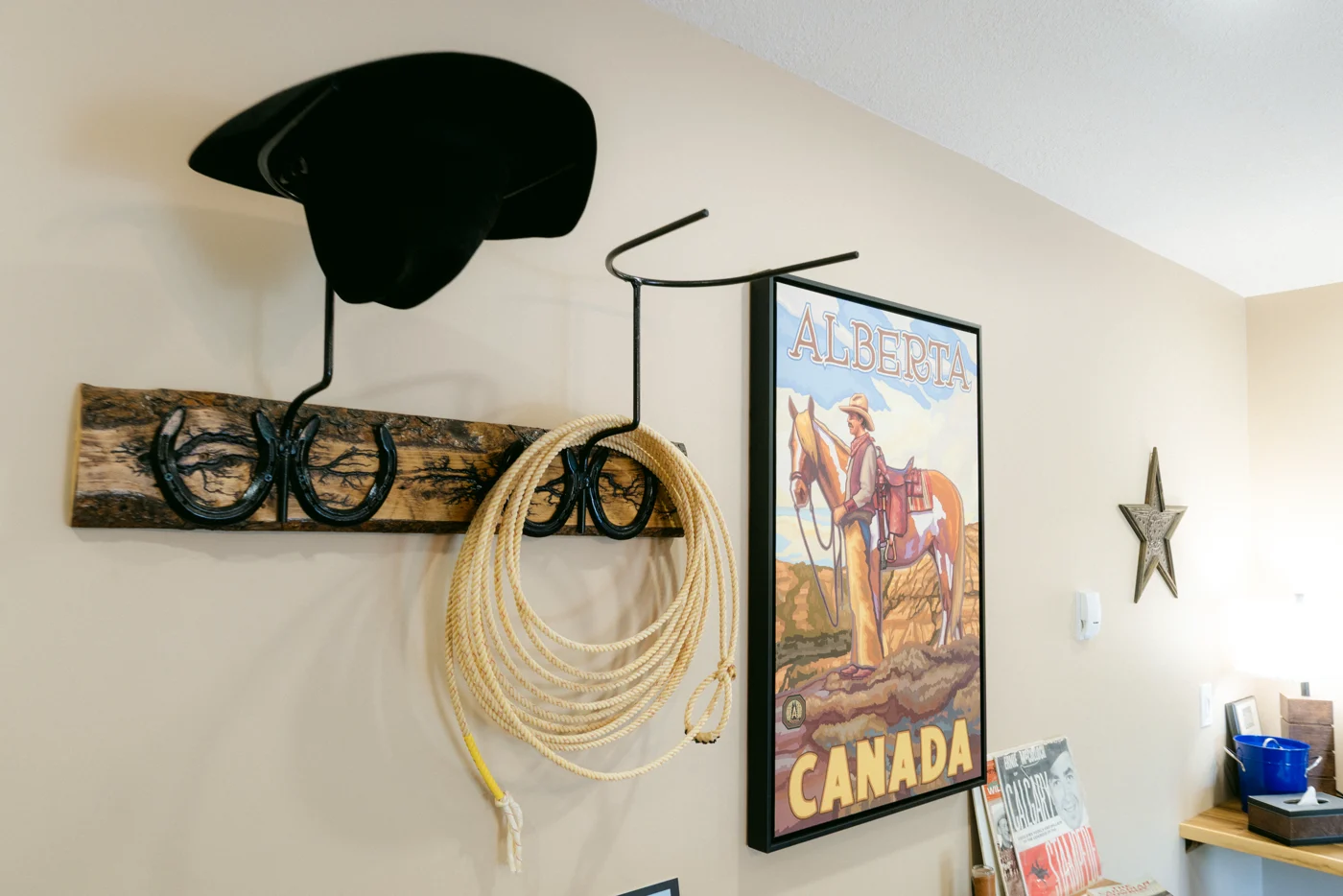 A cowboy hat and coiled rope on a hook beside a vintage travel poster