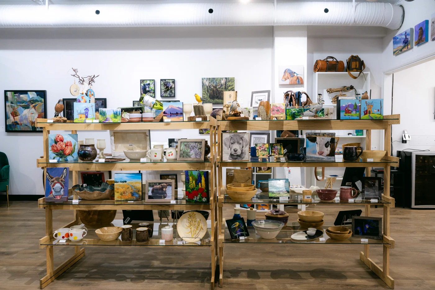 Wooden display shelves of ceramics, bowls and small prints in a gallery shop, paintings on the walls behind