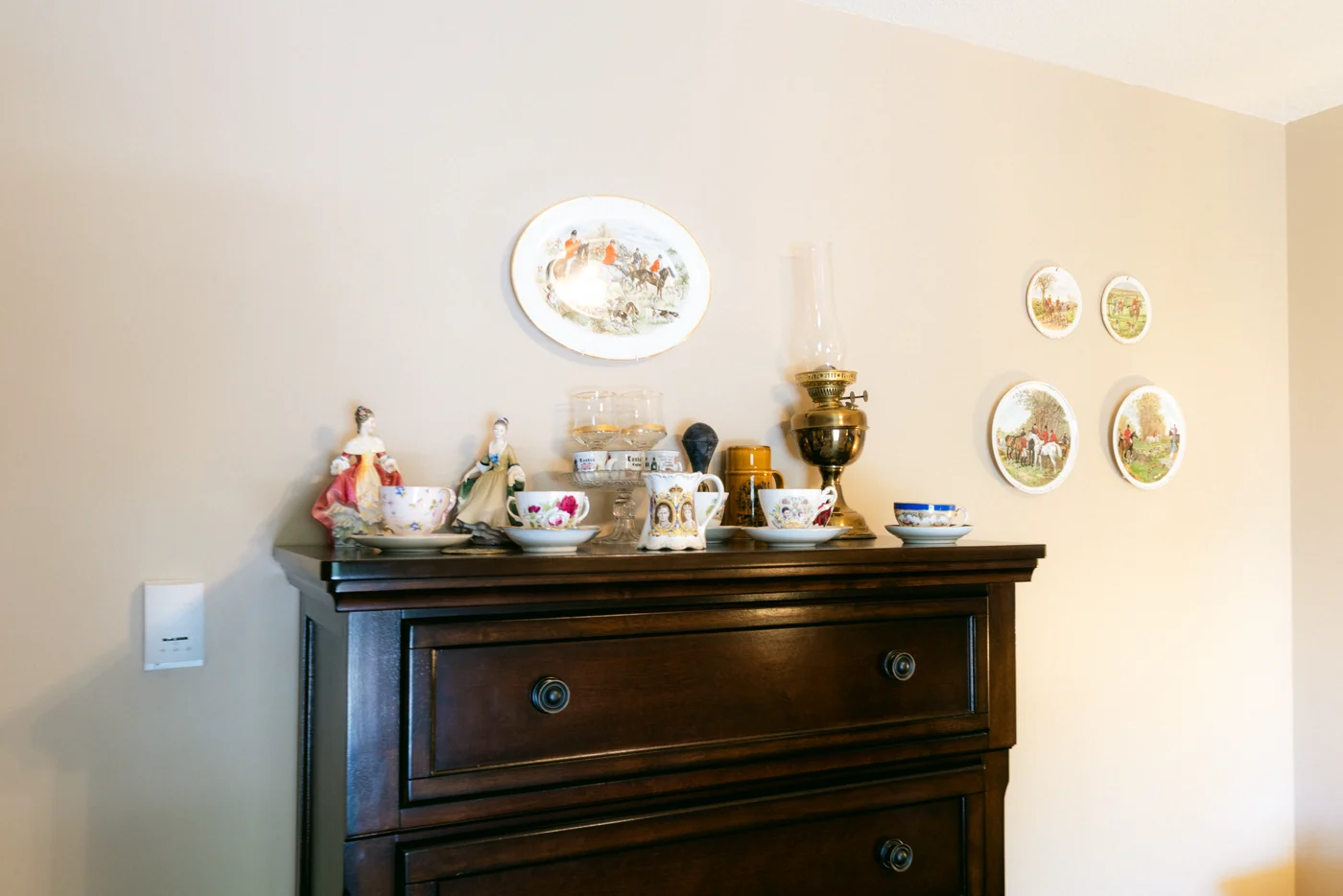 Teacups on a dresser below decorative plates on a wall
