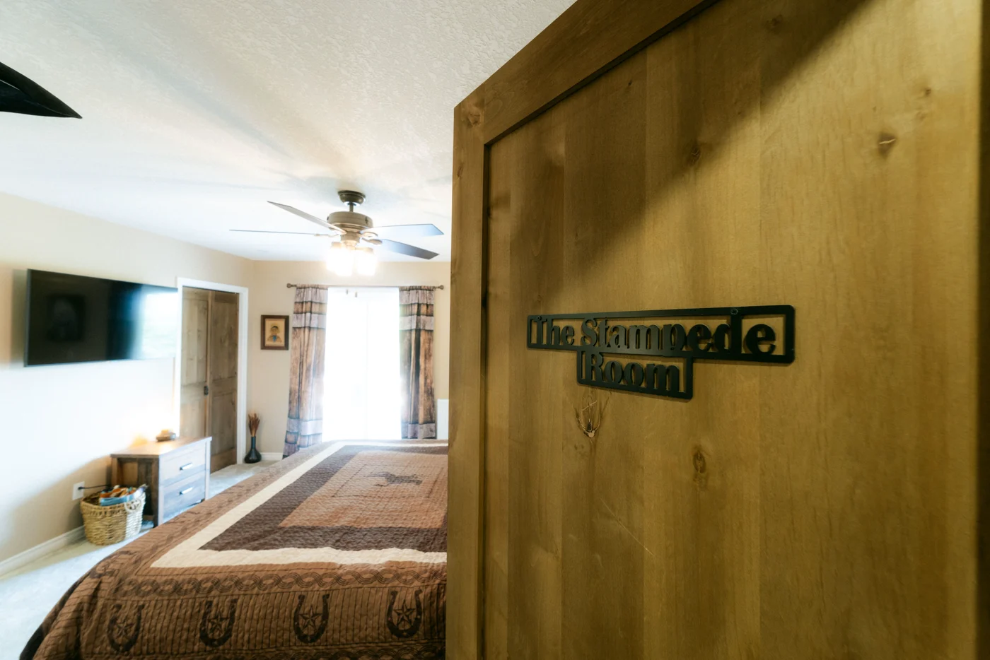 A wooden door with a metal room-name plaque, a quilted bed beyond