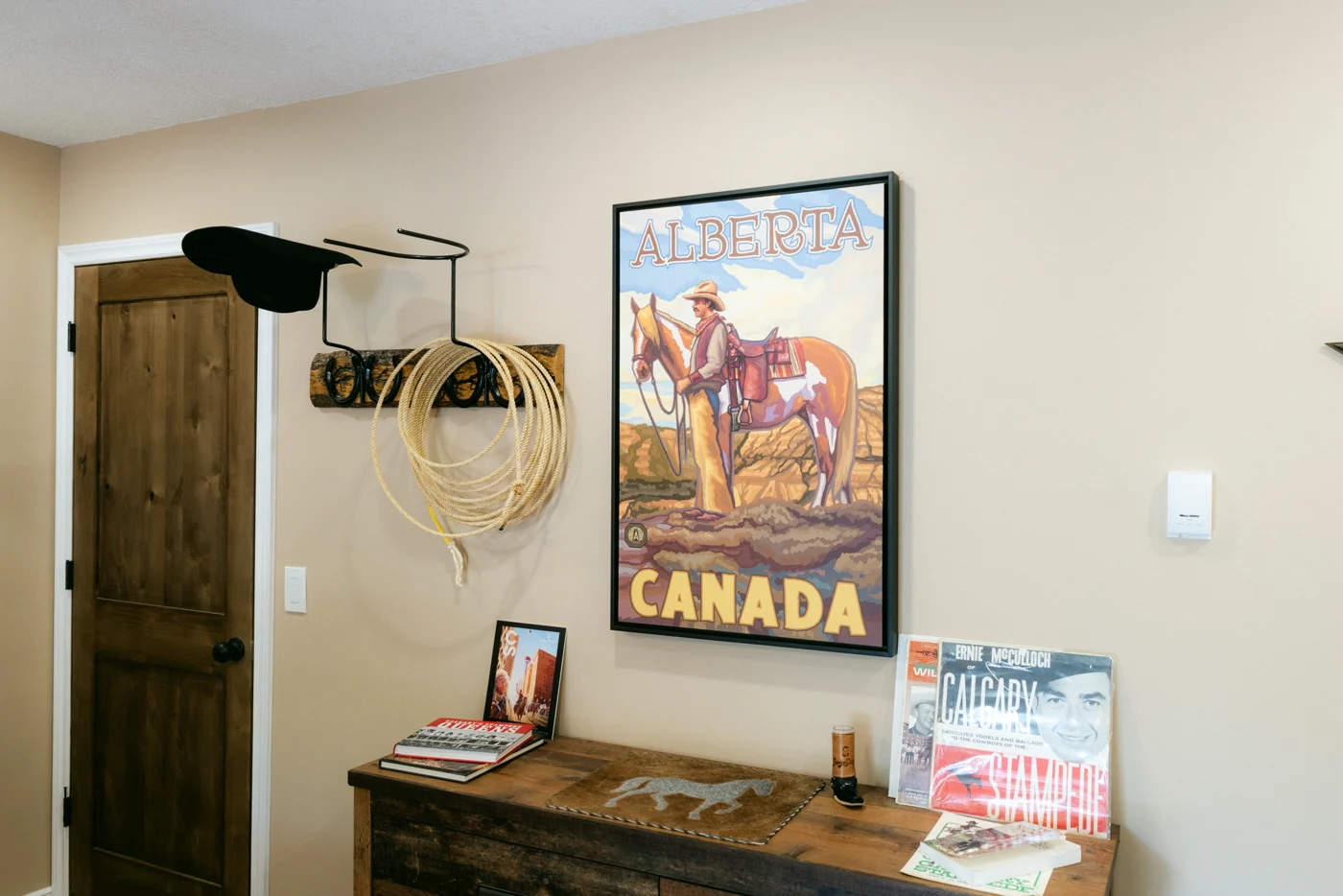 A rustic dresser under a vintage poster, a hat and rope on the wall