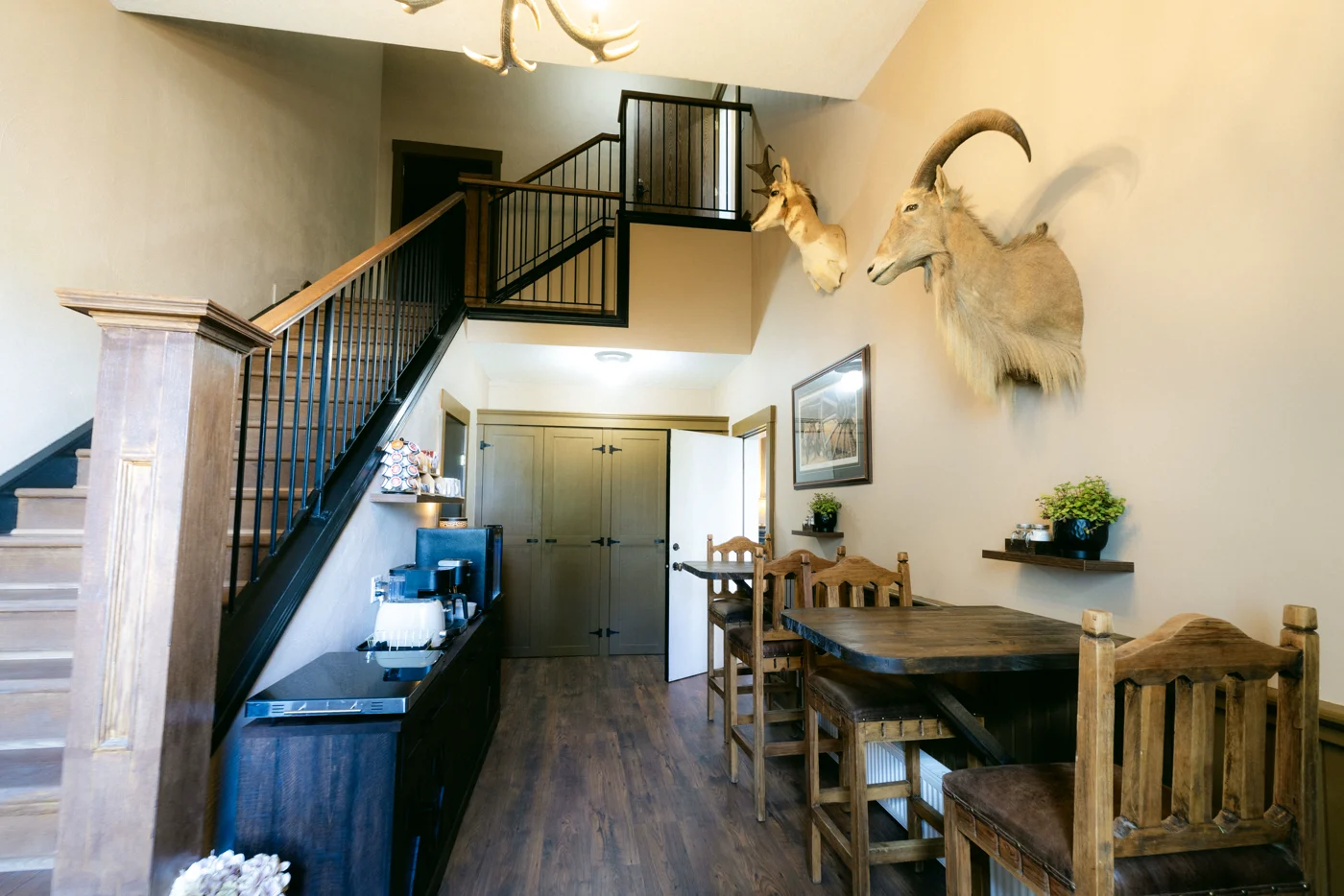A lodge entrance with a staircase, a mounted head and a rustic dining table