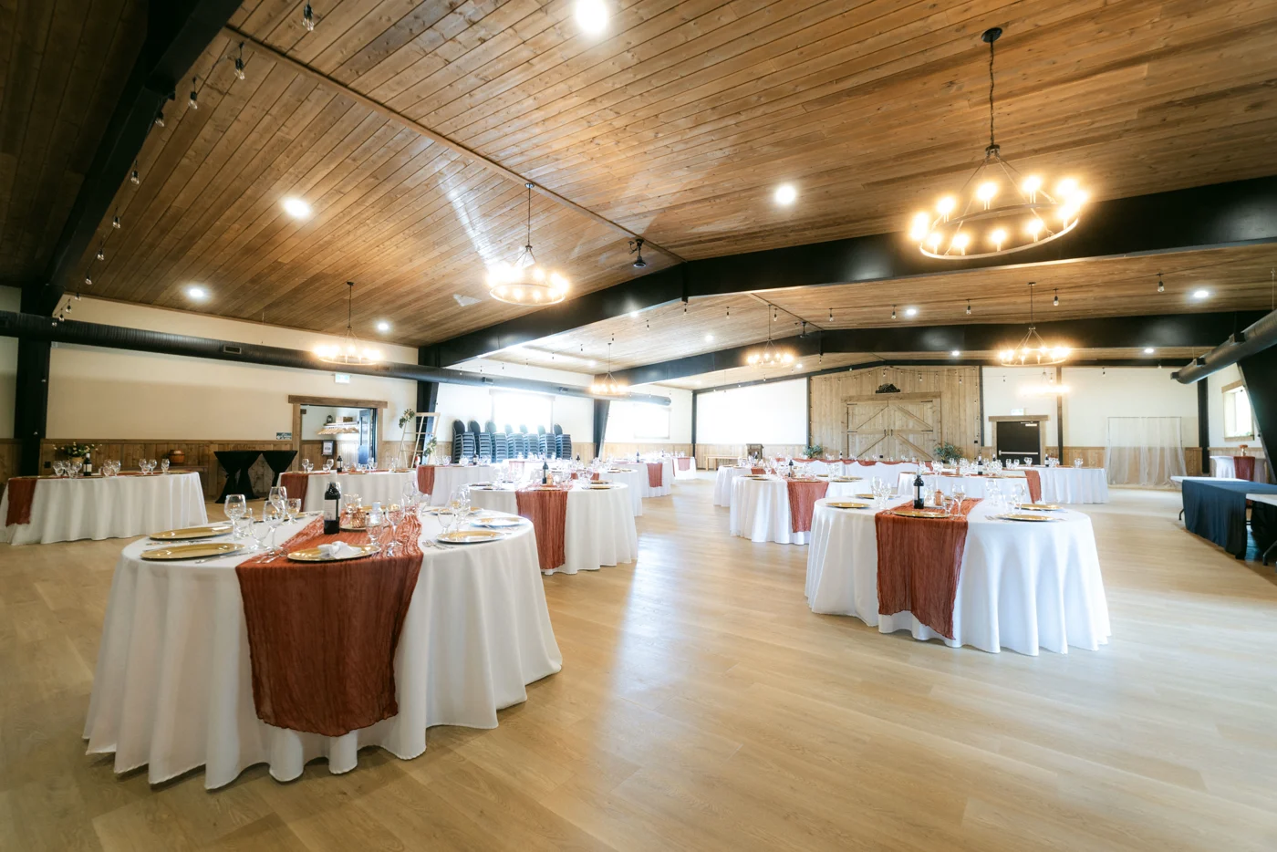 An event hall set with round tables in white linen and rust runners under chandeliers