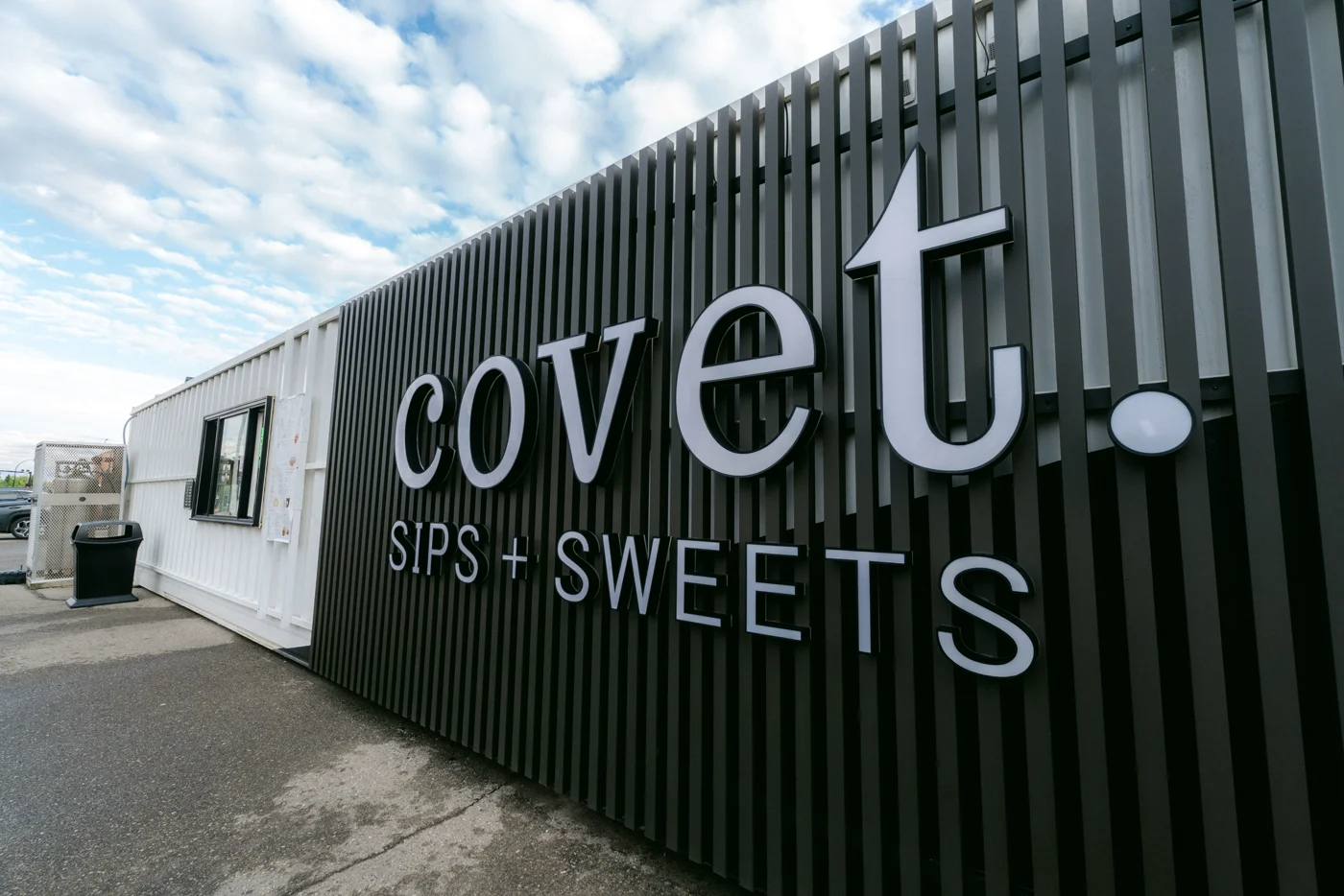 A drinks-and-sweets kiosk's white lettering on a black ribbed wall