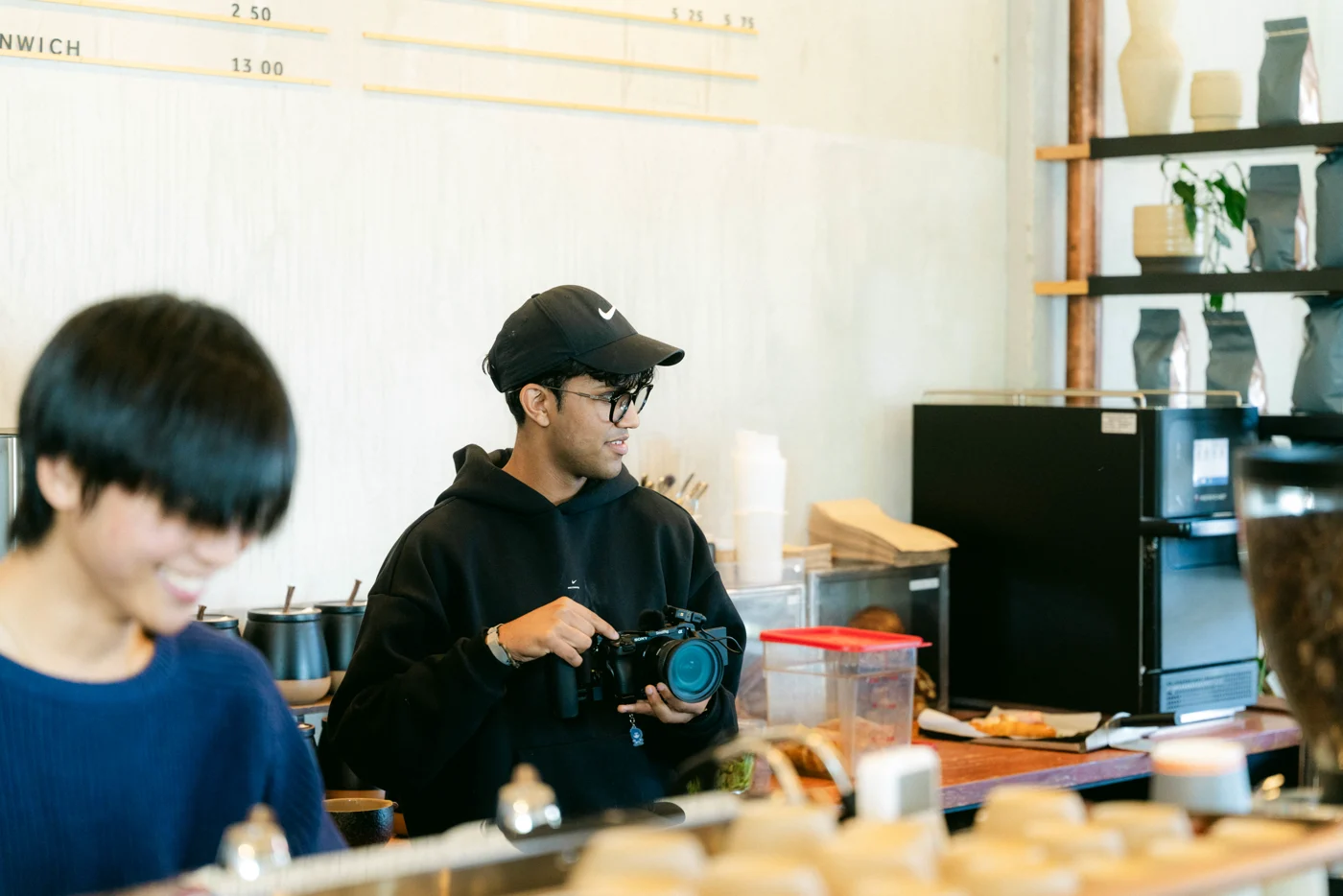 A photographer with his camera stands beside a barista behind the counter of a café