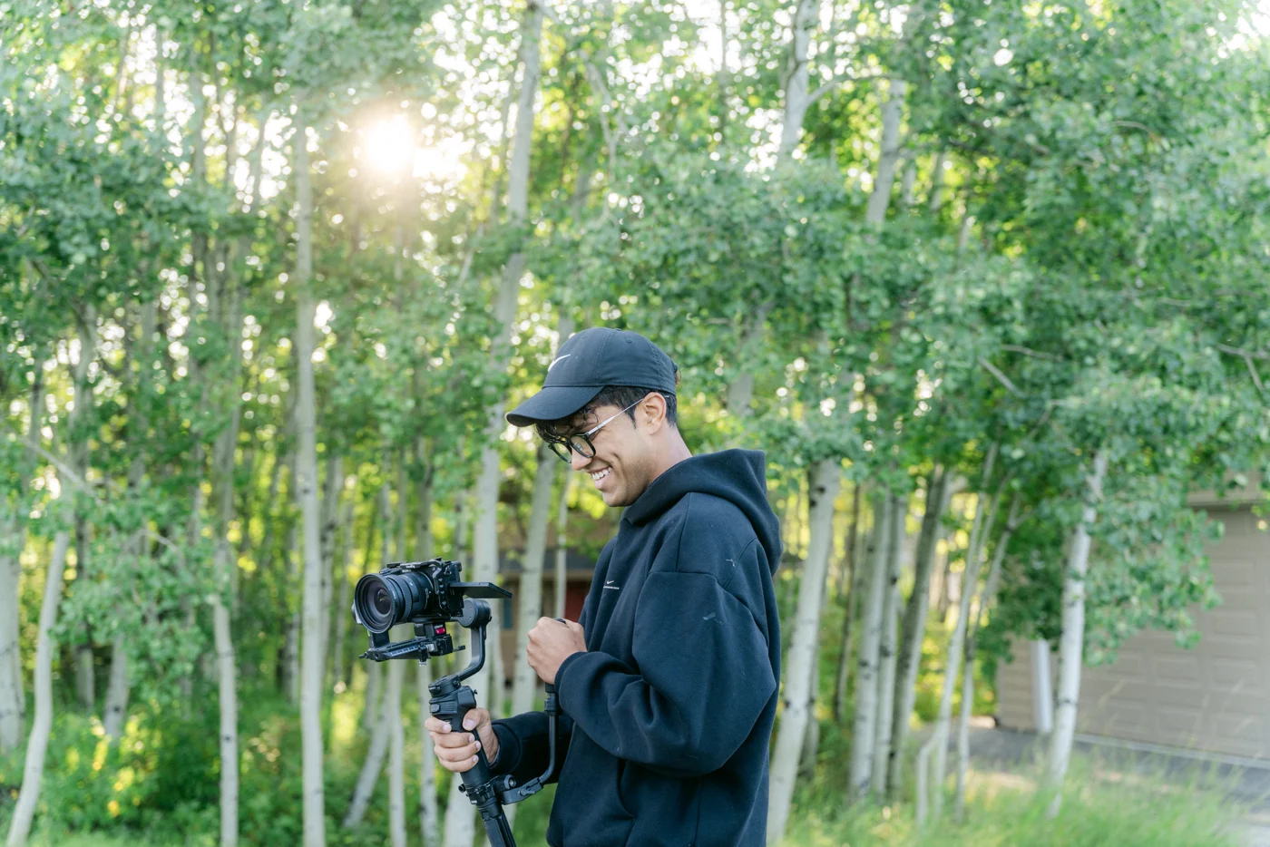 A camera operator with a gimbal rig among backlit aspen trunks