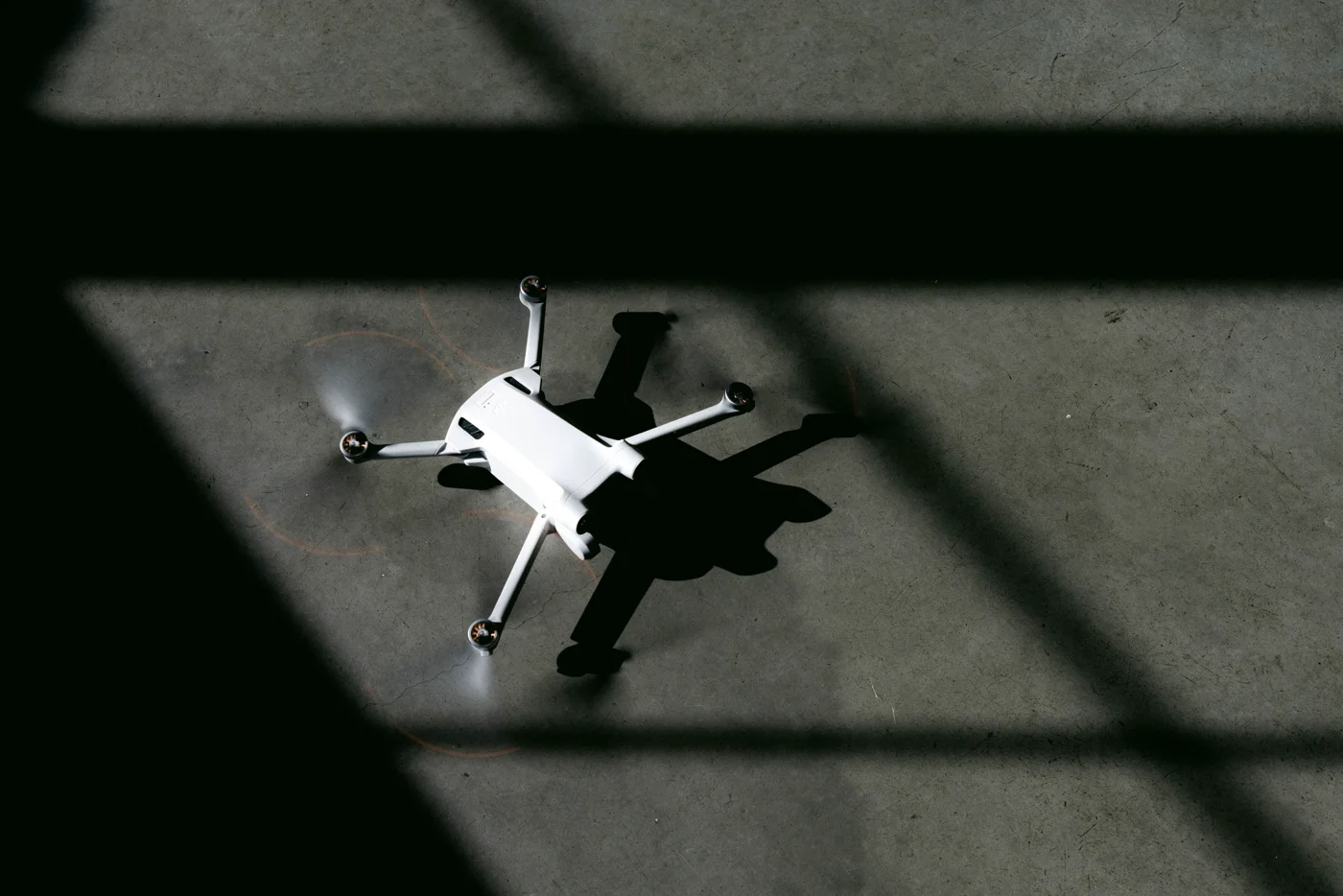 A small drone and its sharp shadow on a sunlit concrete floor, seen from directly above