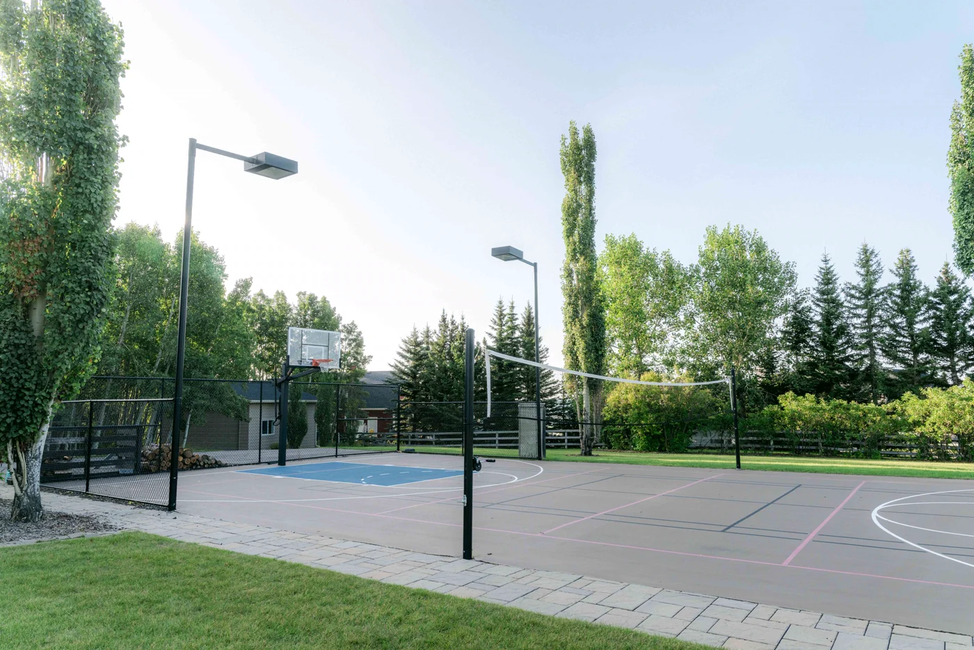 A private sport court with a net, basketball hoop and lights among trees