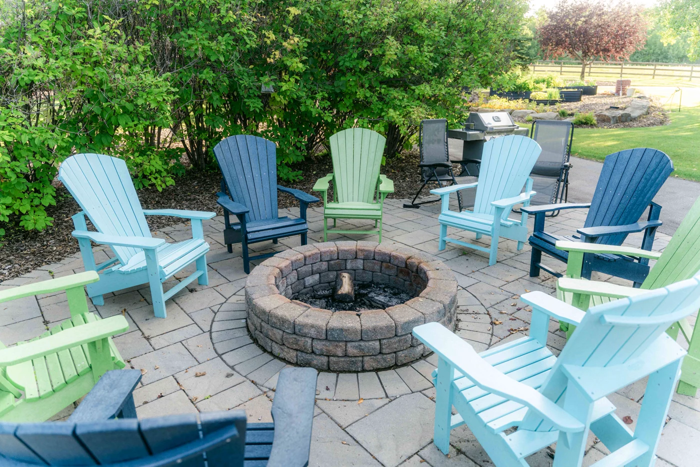Blue, green and black Adirondack chairs around a stone fire pit