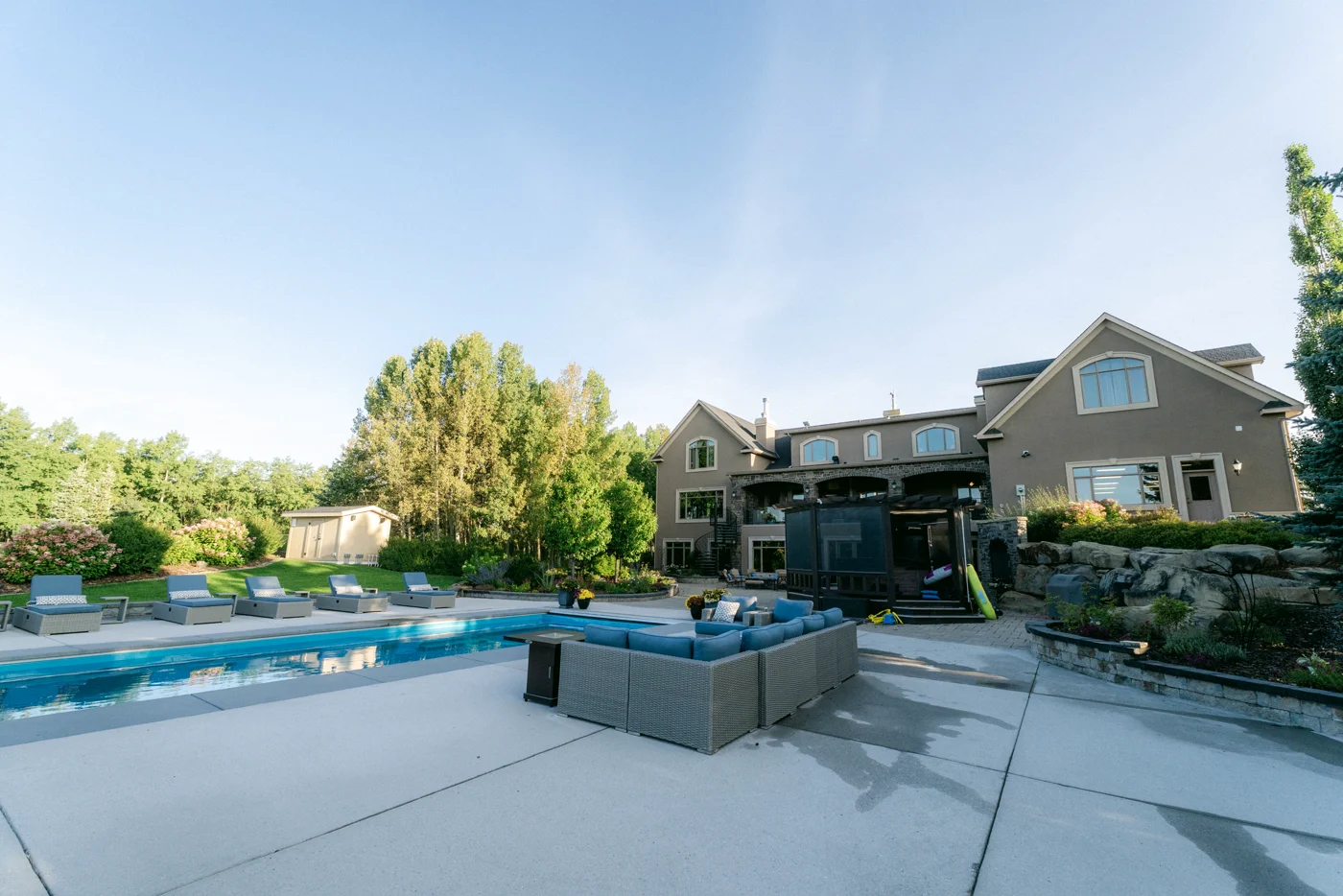 A backyard pool and outdoor sofa on a concrete terrace, the house beyond