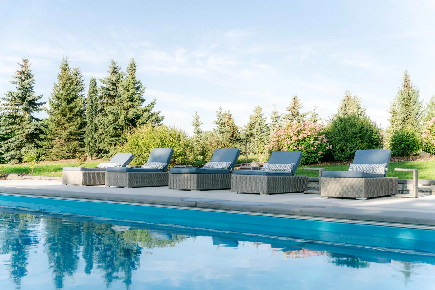 Loungers along a still pool reflecting the spruce trees and sky