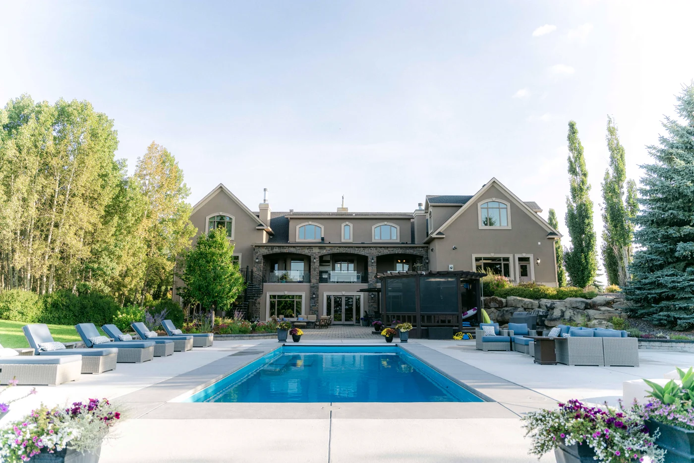 A large house with its pool, loungers and tall poplars, flowers in the foreground
