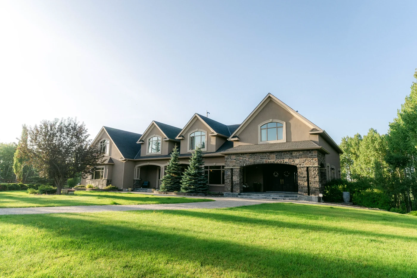 A large stone-and-stucco house across a wide lawn in low evening light
