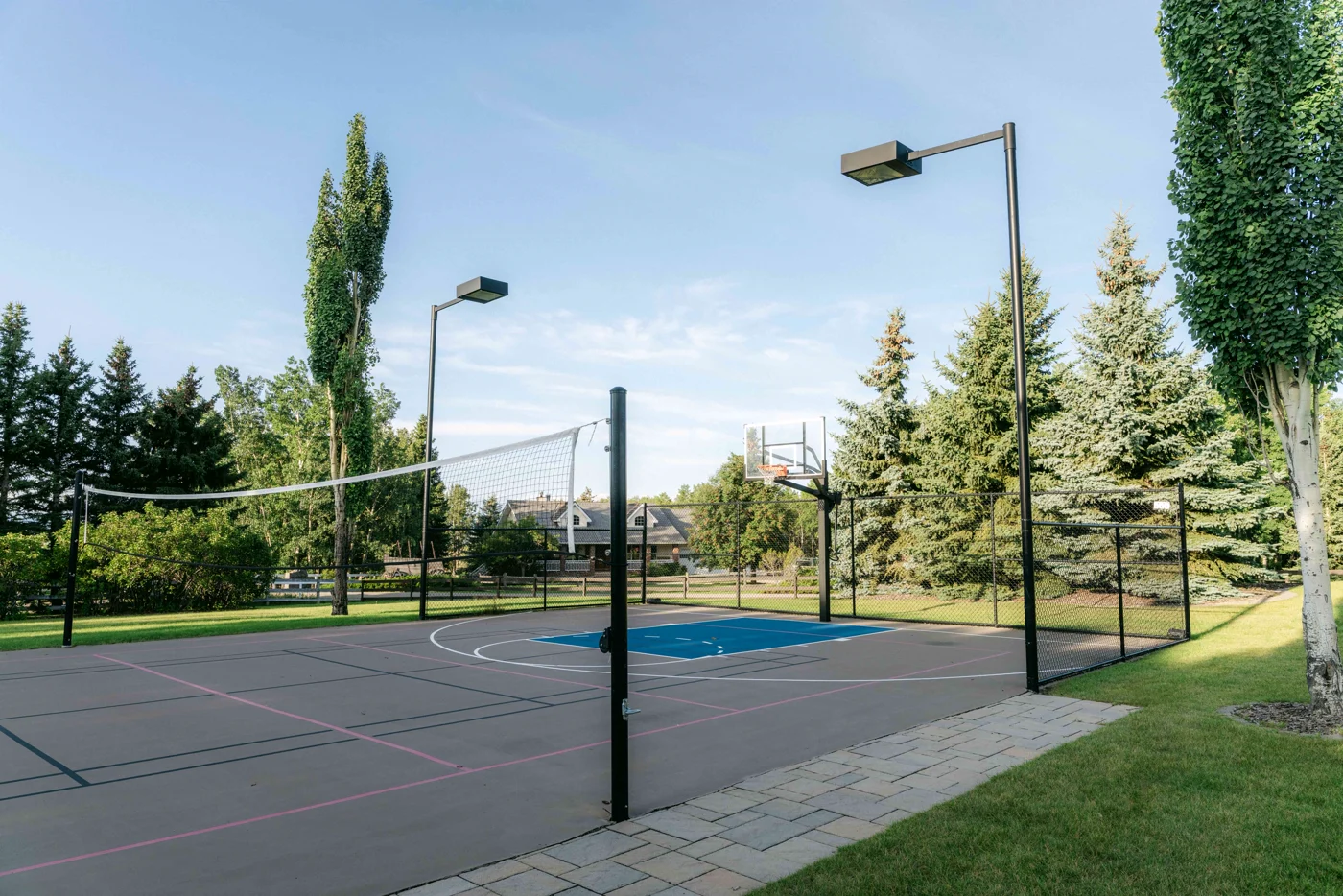 A sport court with a net, hoop and lights seen from the corner