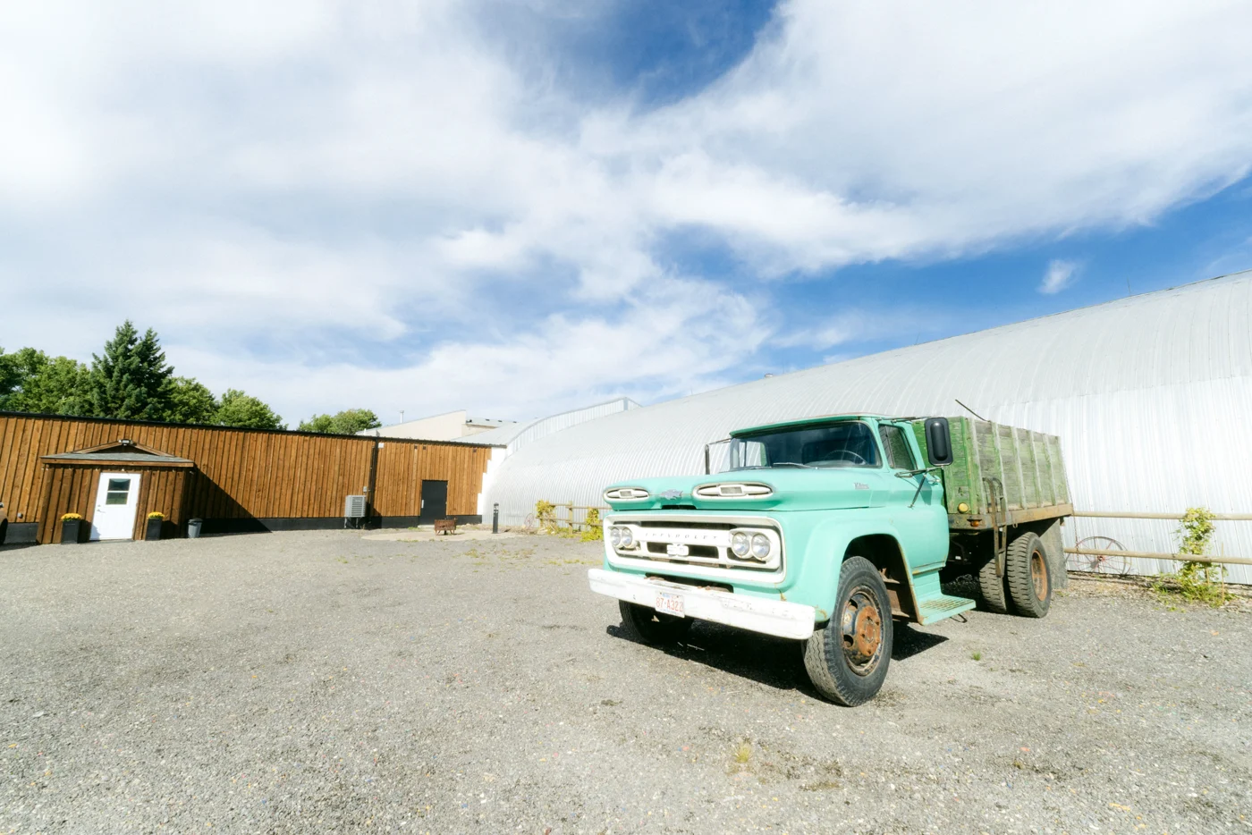 A vintage turquoise farm truck in a gravel yard under a big sky
