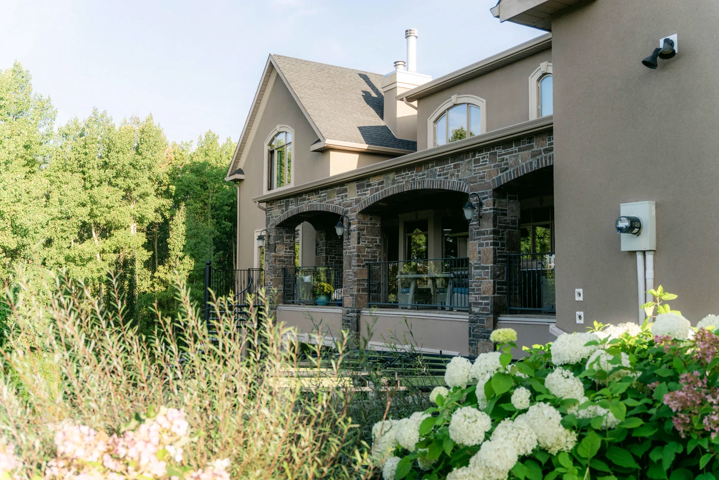 A stone-arched porch of a large house, white hydrangeas in the foreground